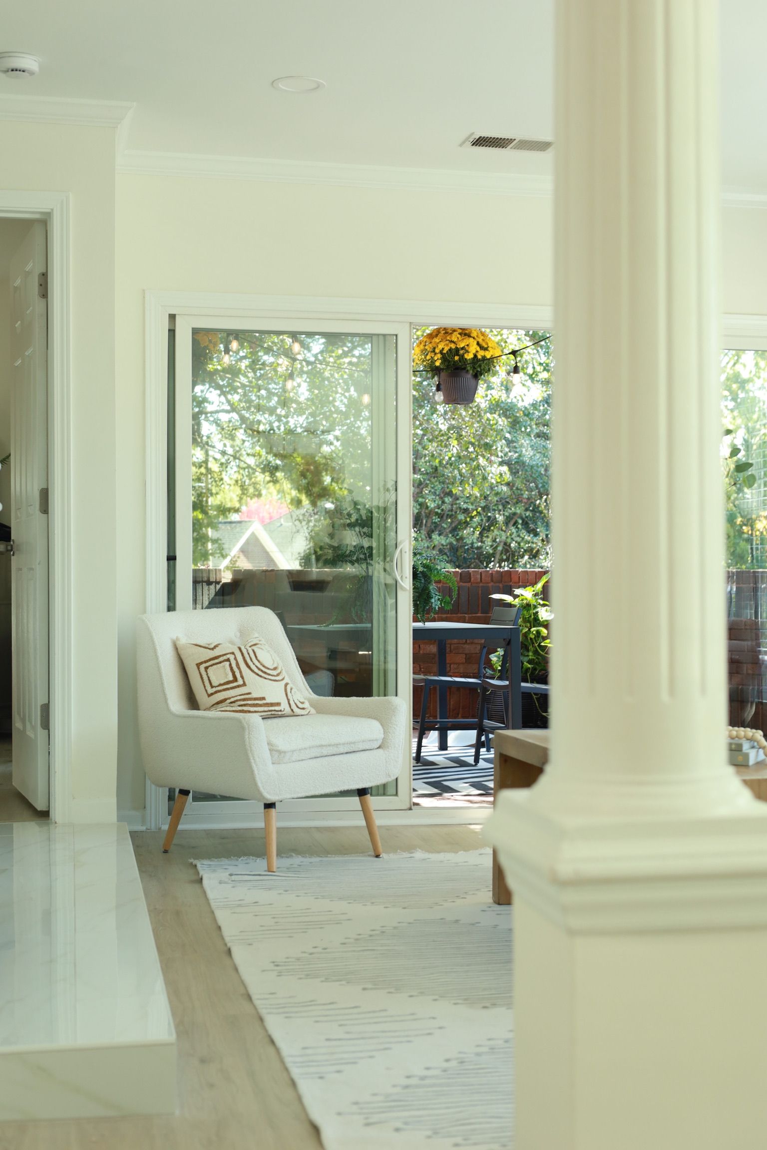 White armchair in a bright room, facing a sliding glass door to a balcony. A column is in the foreground.