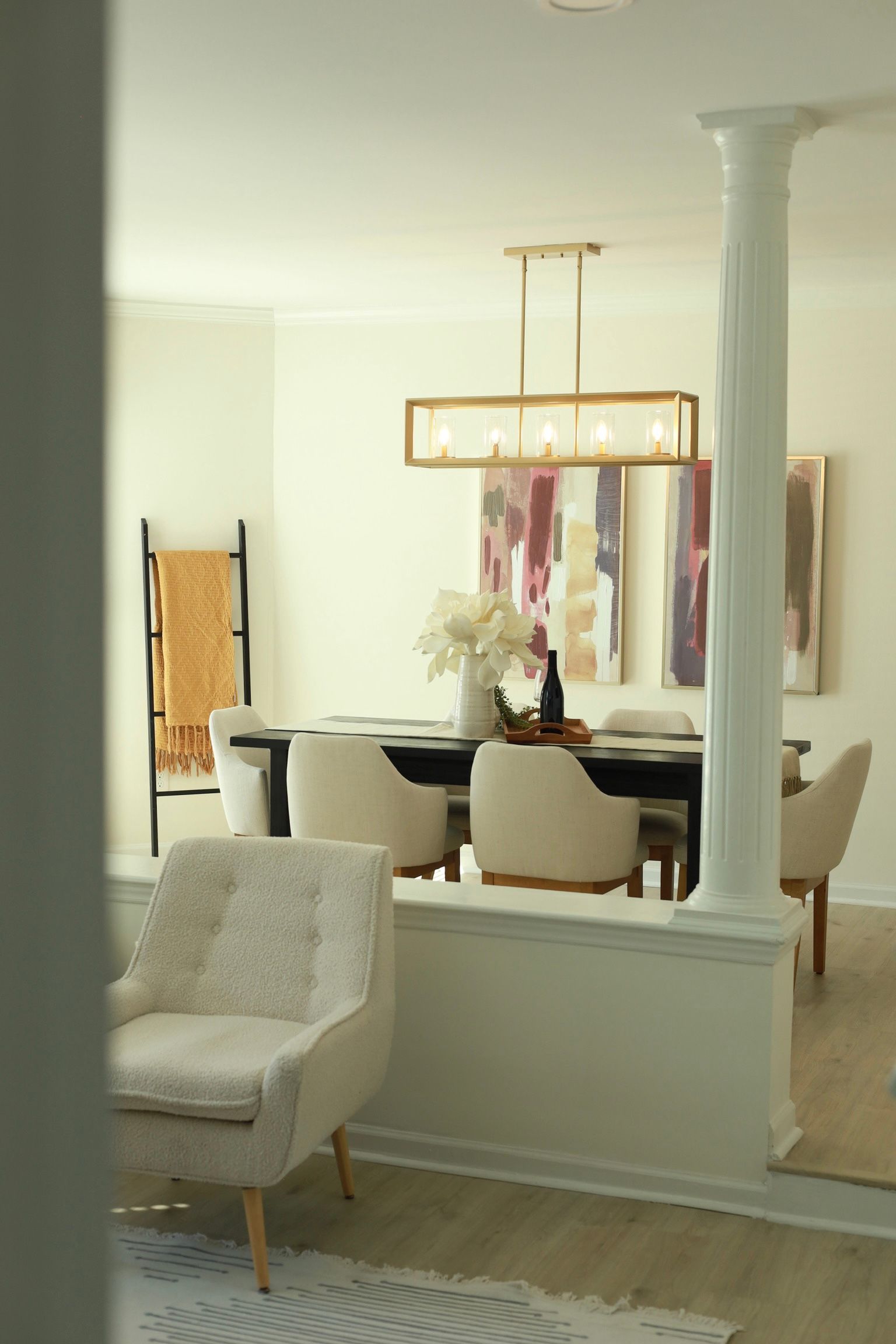 Dining area with dark table, cream chairs, art, and a gold light fixture. A cream armchair is in the foreground.