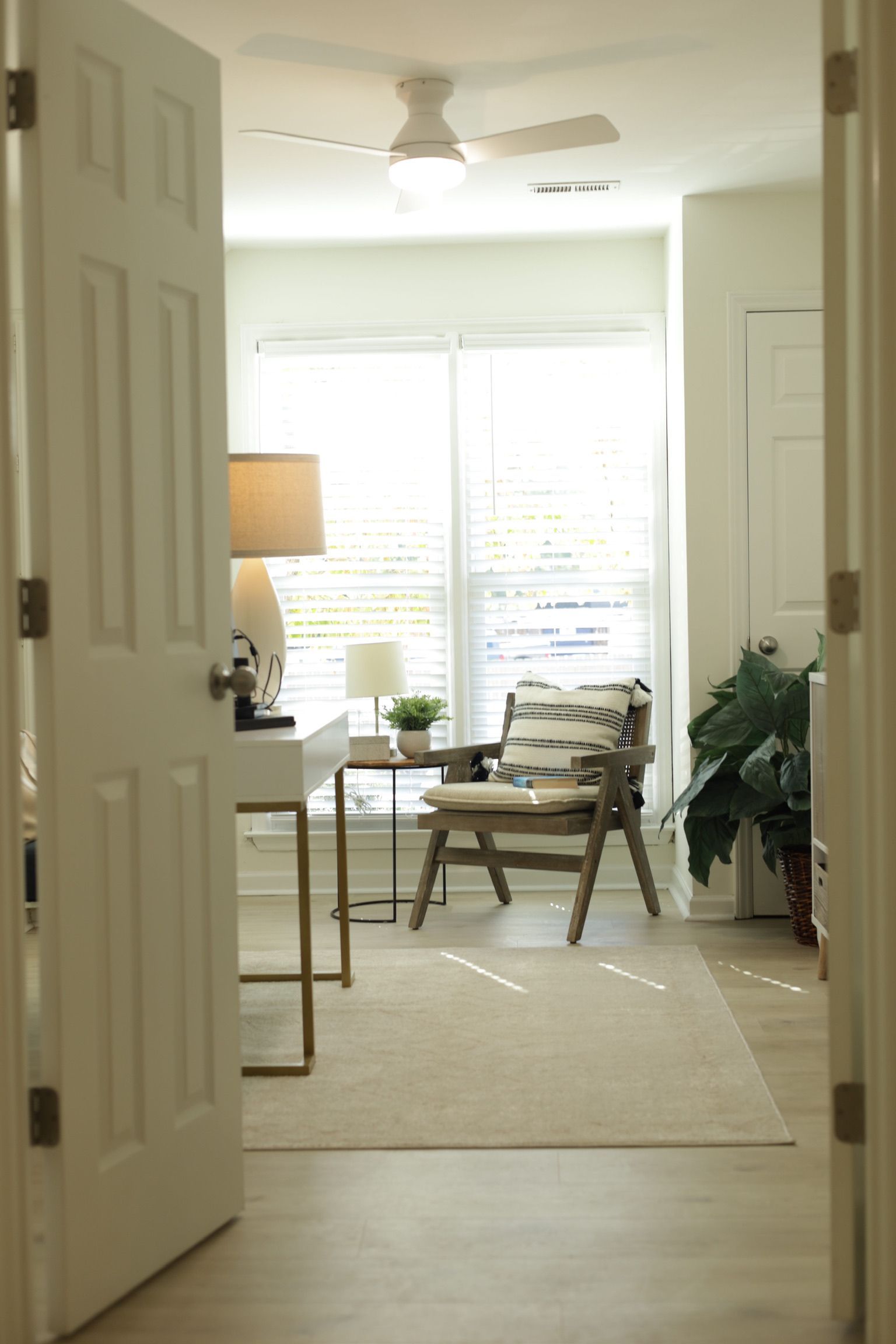 Open white door leading to a home office with desk, chair, and large windows.