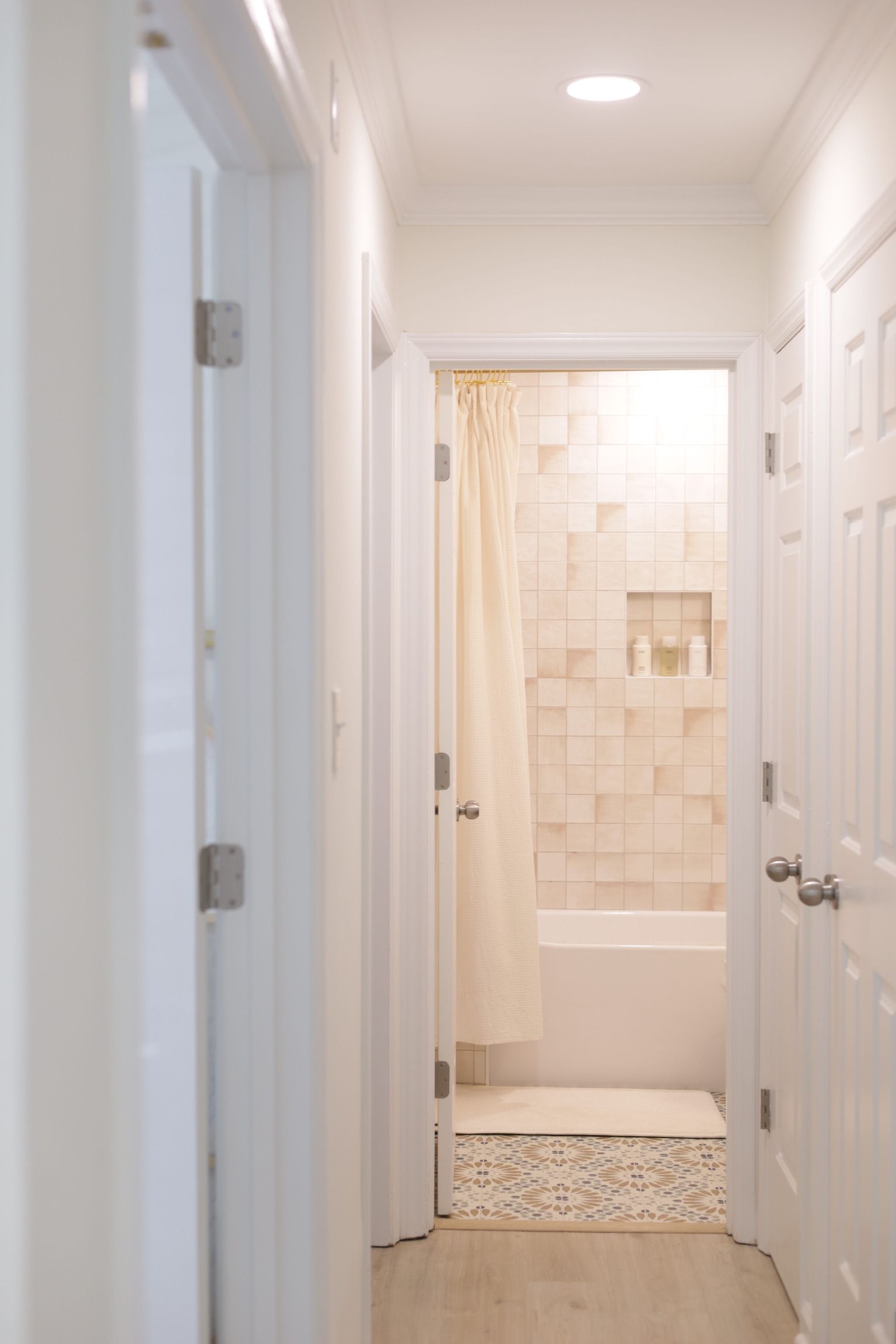 Hallway with white doors and a partially visible bathroom with a tub and tile.