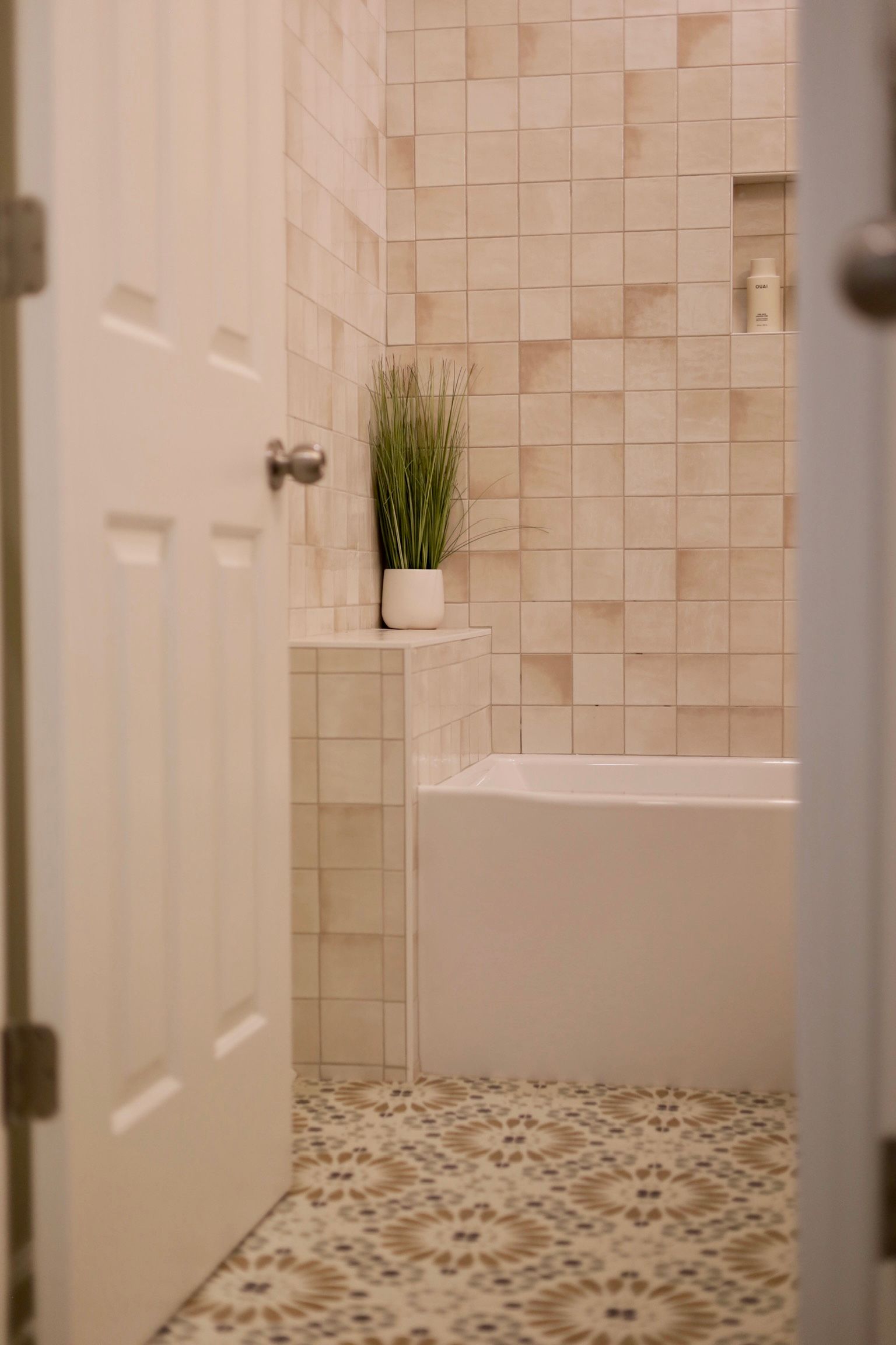 Bathroom interior with beige textured tile walls, a white tub, and patterned floor tiles.