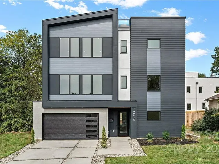 Modern three-story house with gray and white siding, black garage door, and concrete driveway.
