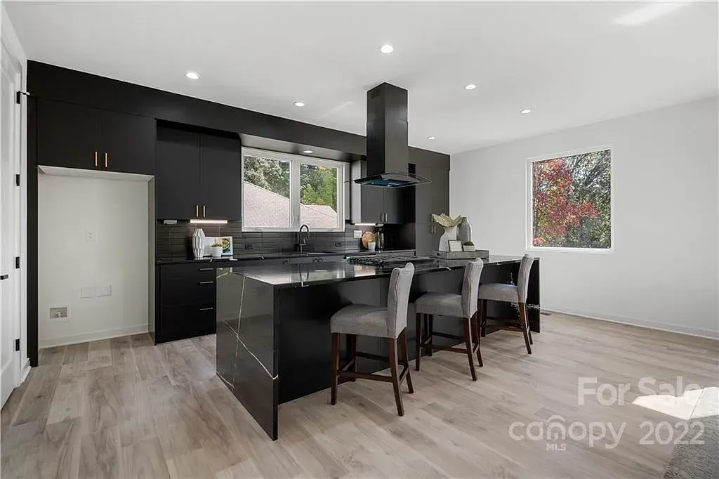 Modern black kitchen with island, gray stools, and light wood floors.