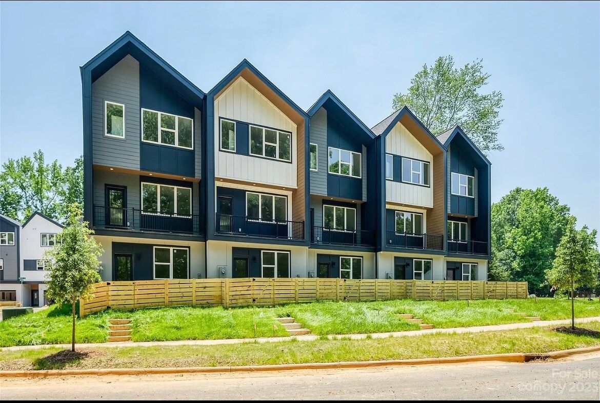 Row of modern townhouses with black and beige exteriors, set on a grassy hill.