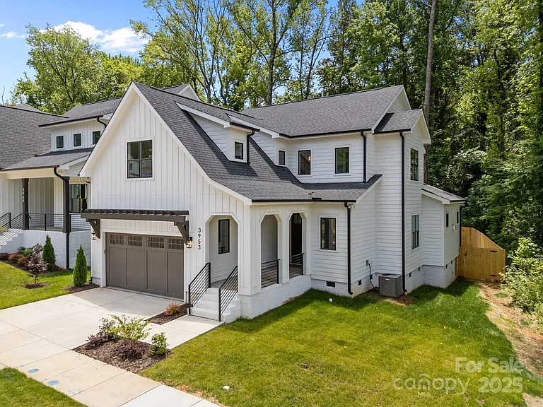 White farmhouse-style home with black trim, two-car garage, and lush green lawn.