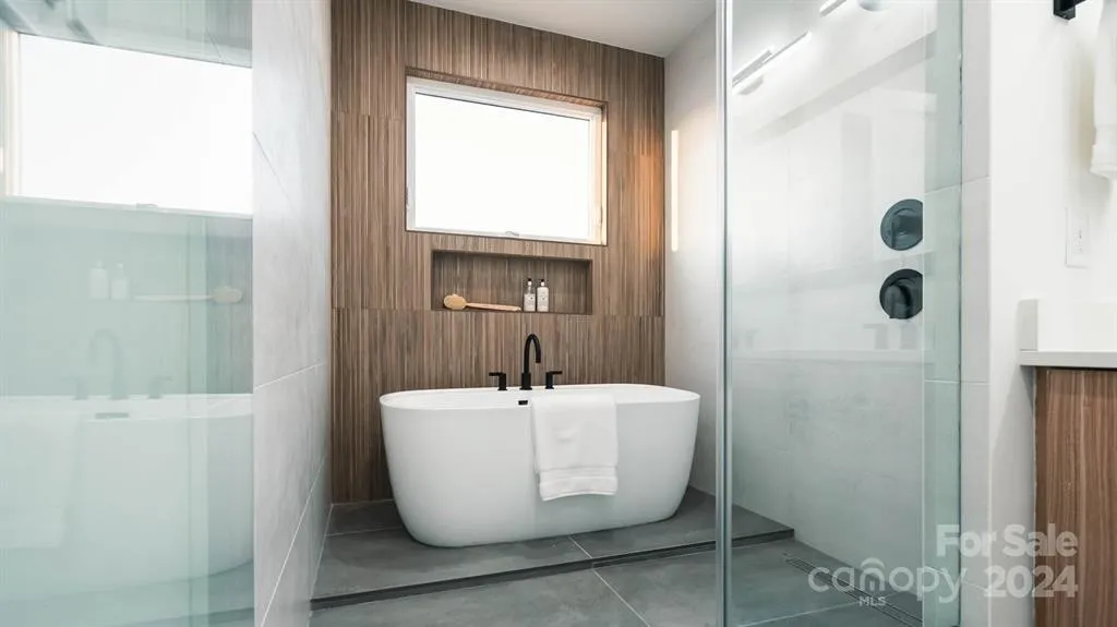 Modern bathroom with a freestanding tub, shower, wood accent wall, and window.