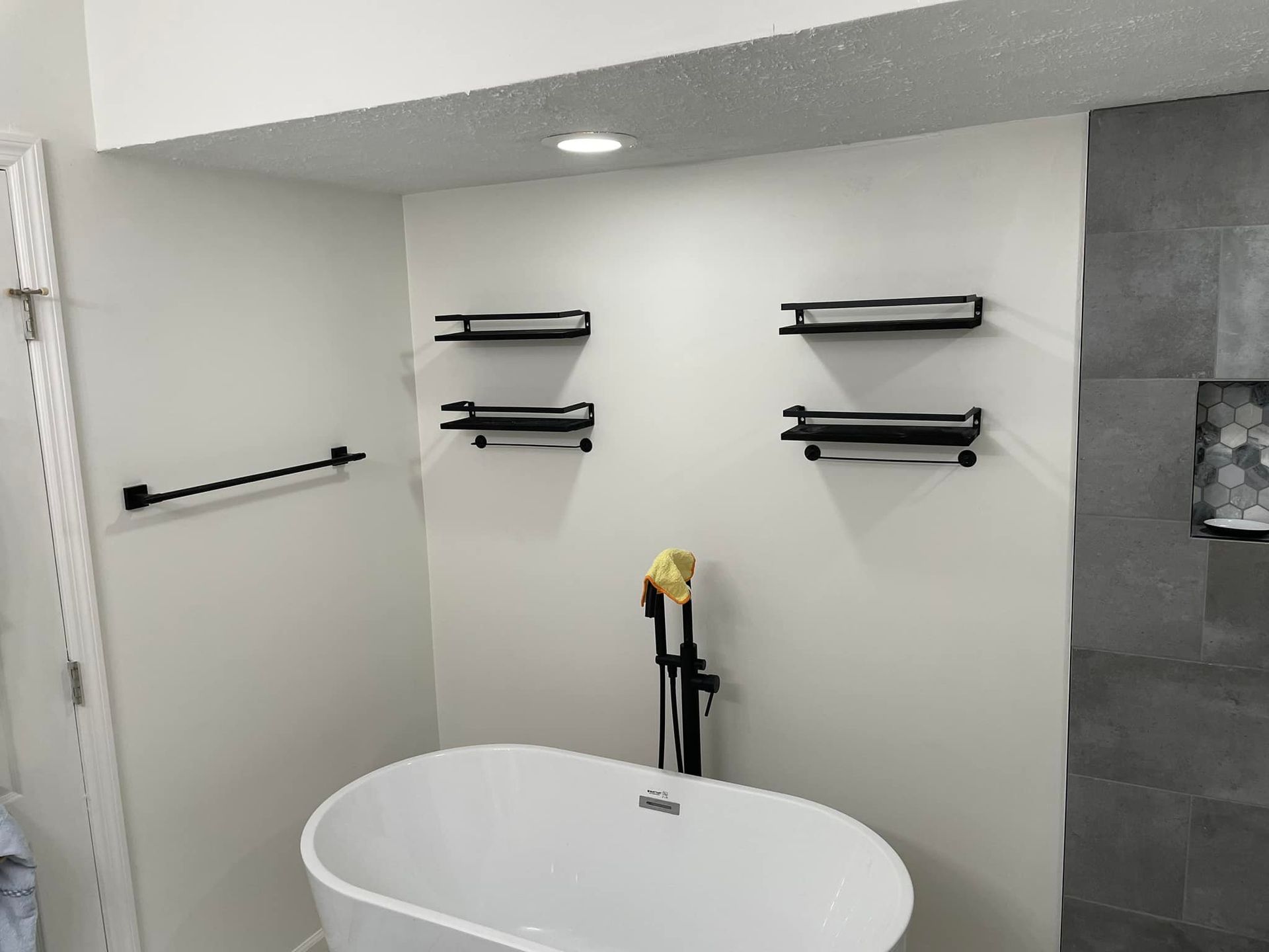 Modern bathroom with a freestanding tub, wall shelves, towel bars, and dark tile shower wall