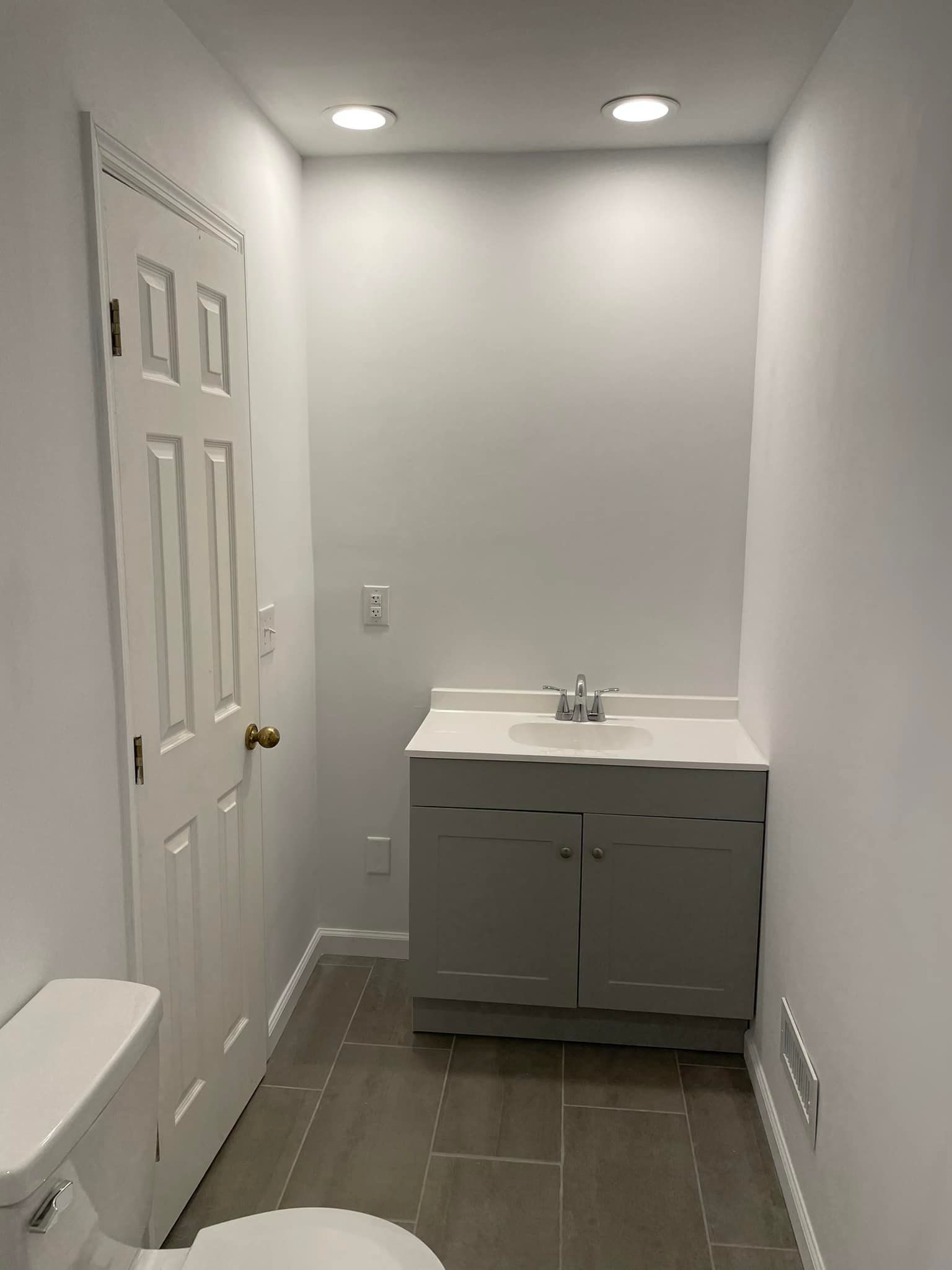 Small bathroom with white vanity, sink, mirror, and recessed lights on gray tile floor.