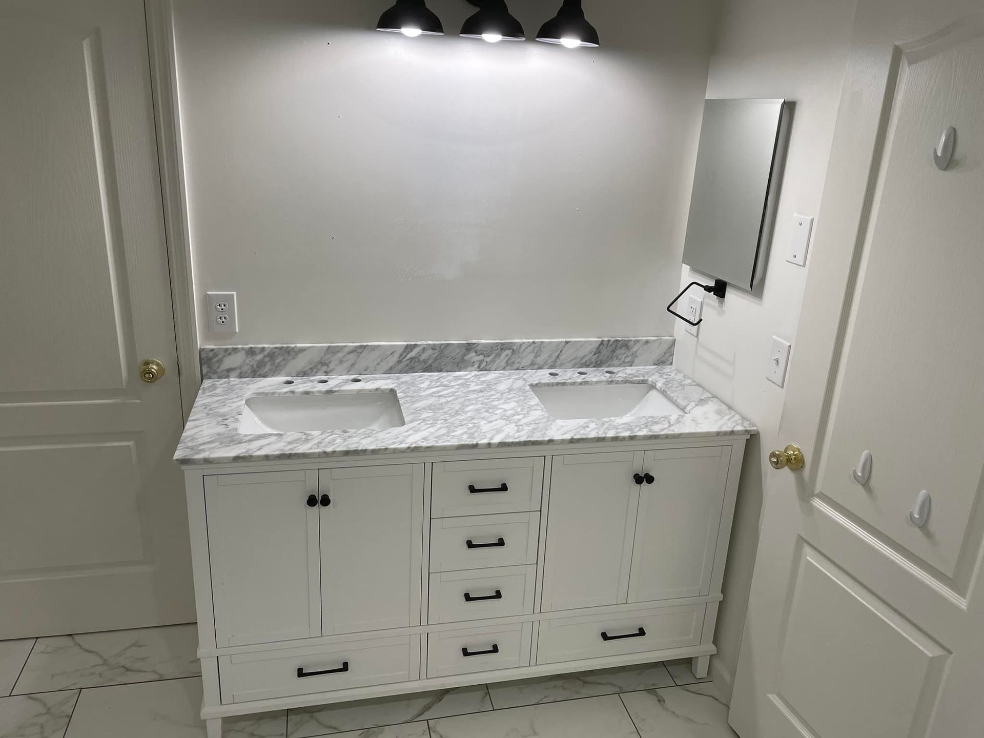 White bathroom vanity with marble countertop, double sinks, mirrored medicine cabinet, and wall lights