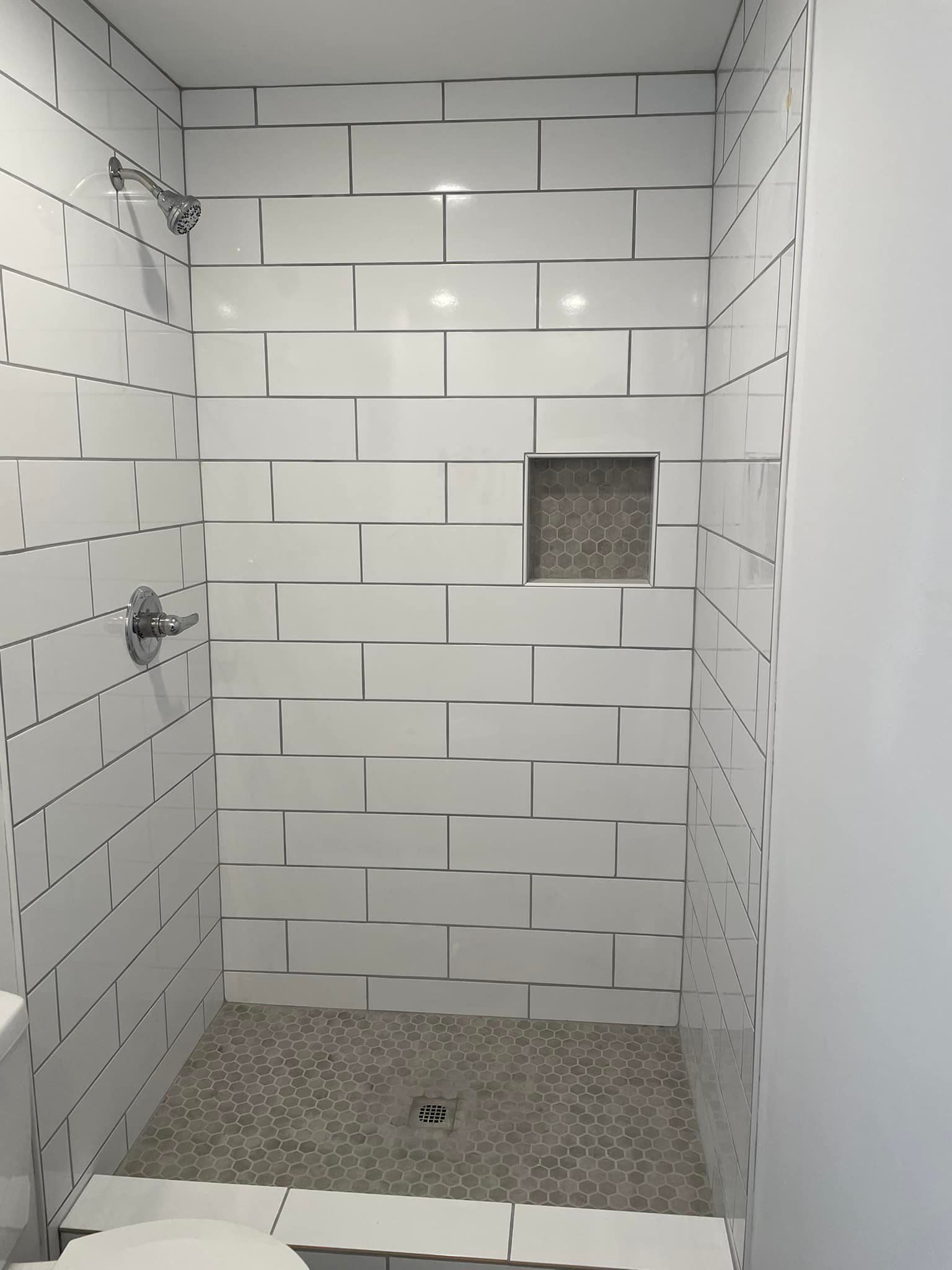Empty tiled shower stall with a small square niche and pebble floor drain area.