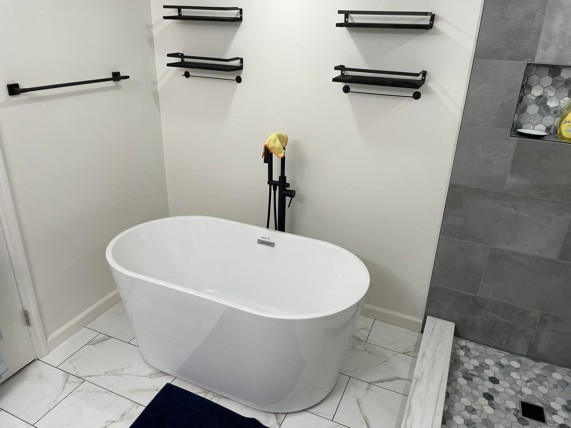 Modern bathroom with a white freestanding tub, black towel racks, and tiled shower area