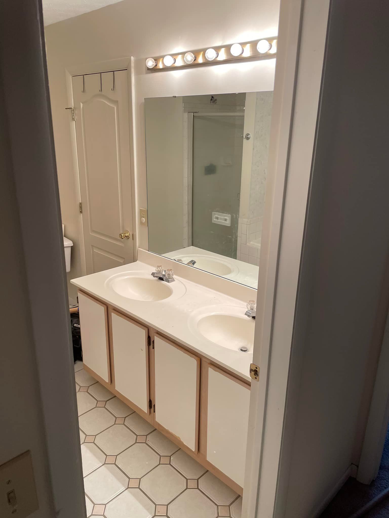 Bathroom vanity with two sinks, large mirror, and overhead lights in a beige-tiled room