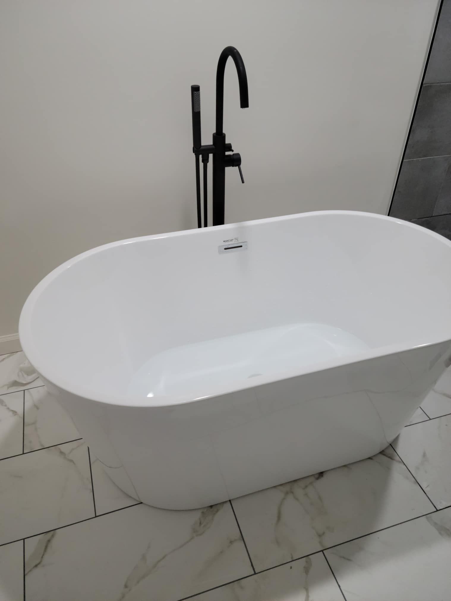 White freestanding bathtub with black faucet on tiled bathroom floor