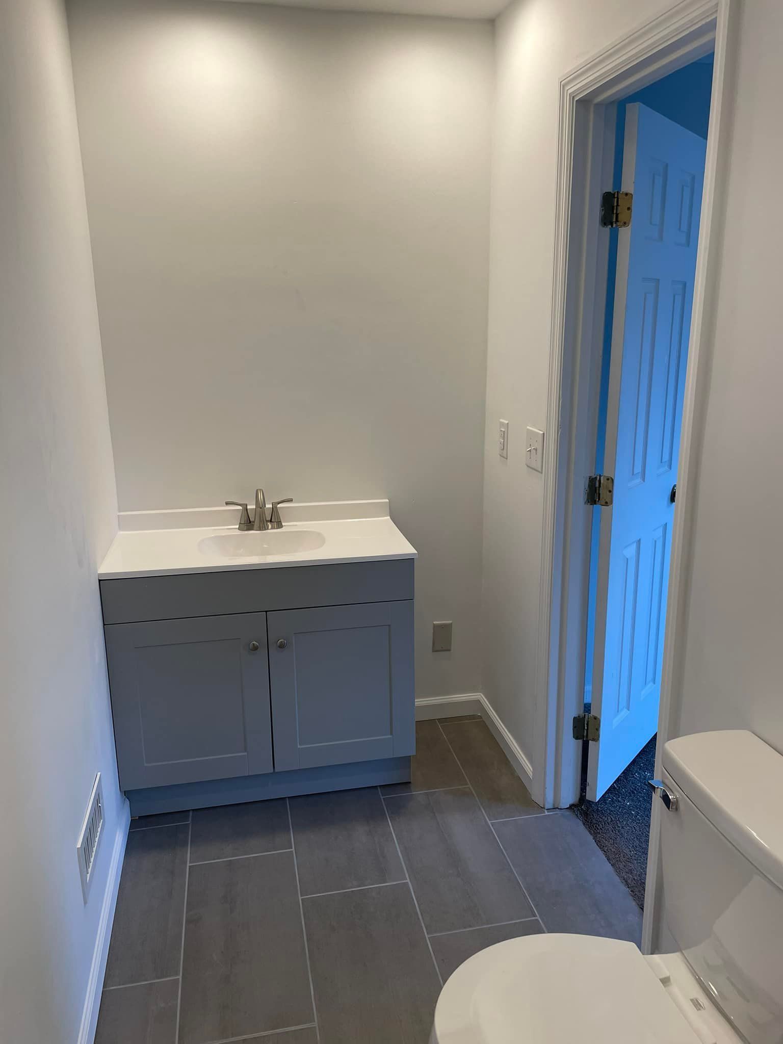 Small bathroom with white vanity, sink, toilet, and blue-tinted shower or doorway.