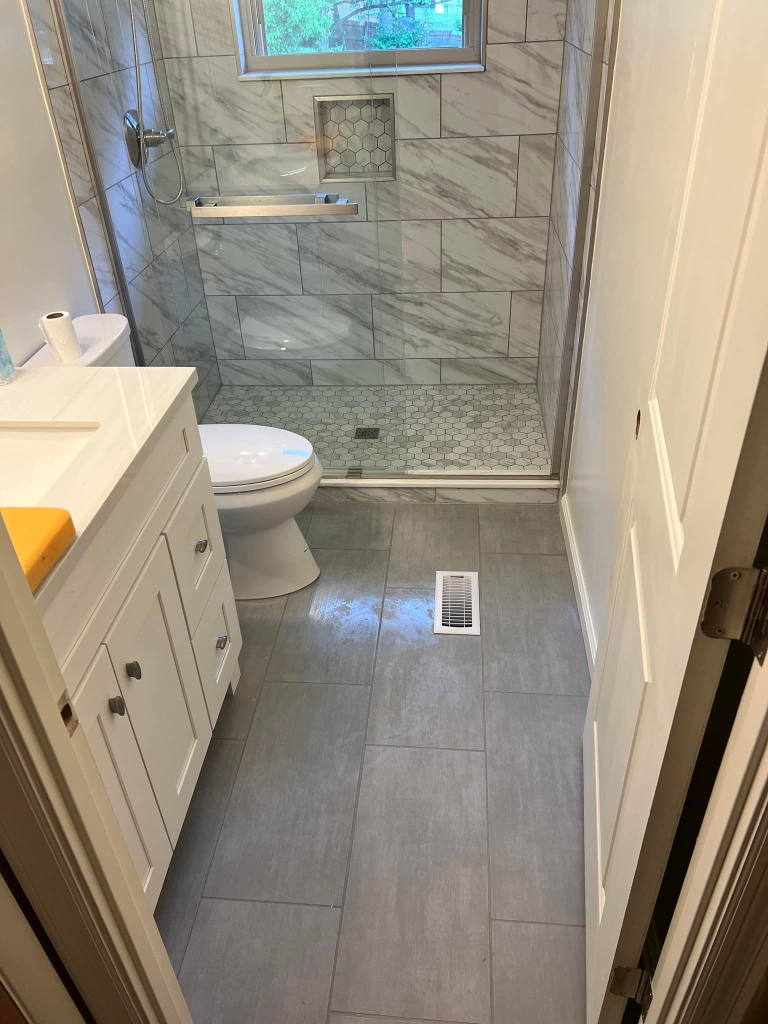 Small bathroom with tiled shower, toilet, white vanity, and gray floor, viewed from the doorway