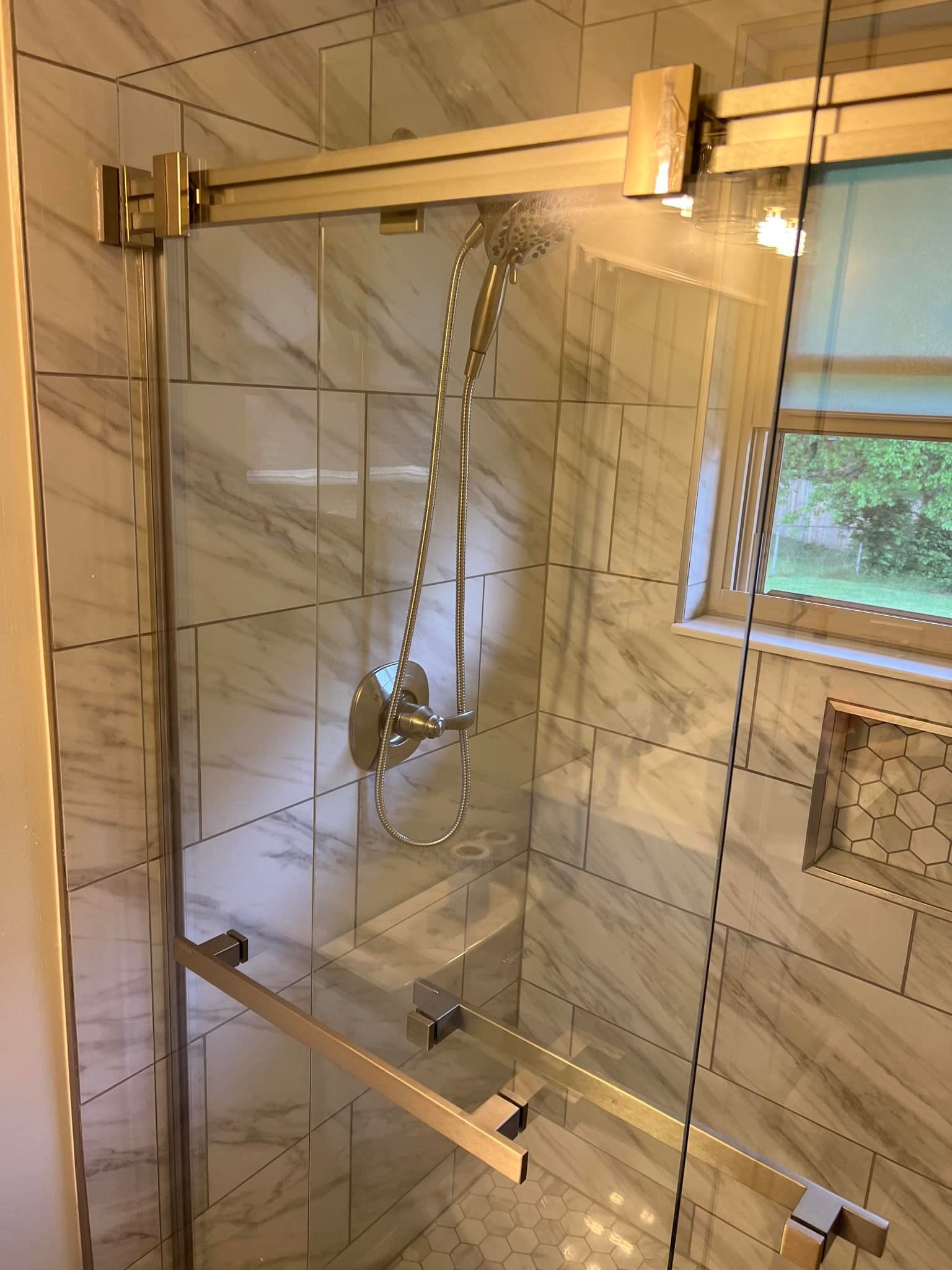 Glass shower enclosure with chrome grab bars and a tiled bathroom wall рядом a window