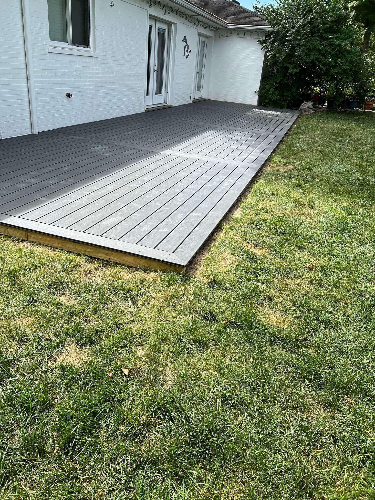 White deck beside a house with a grassy lawn and a tree in the yard