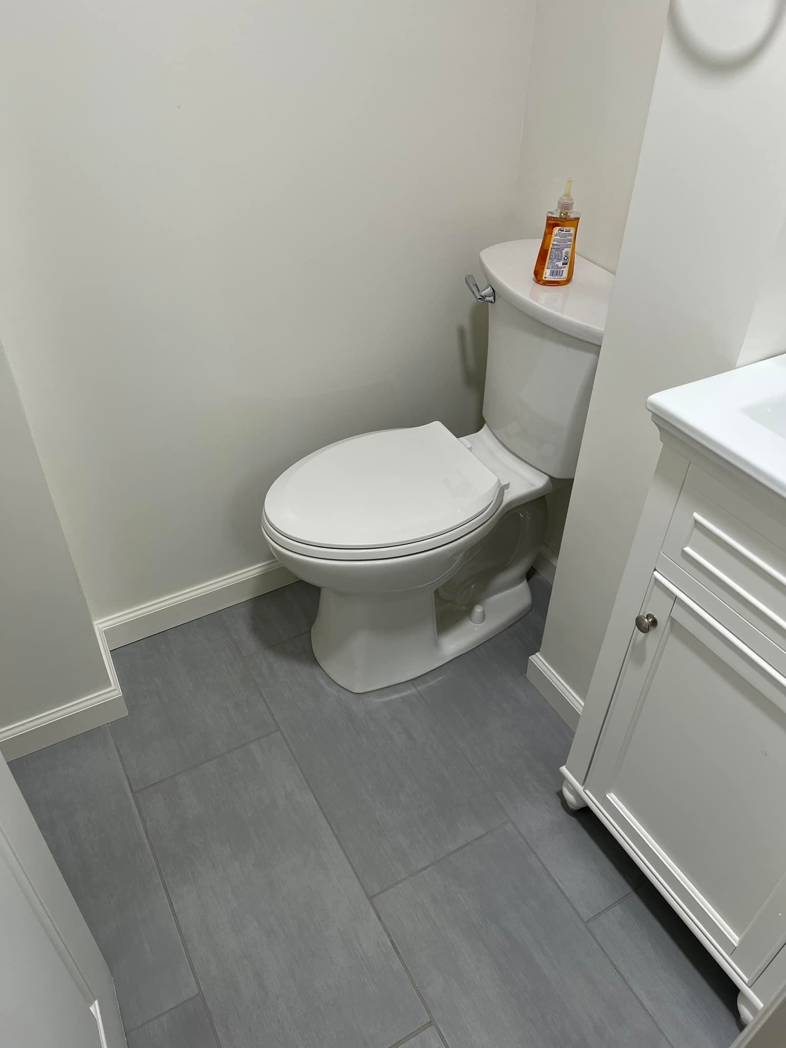 Small white bathroom with a toilet, gray tile floor, and a sink cabinet on the right.