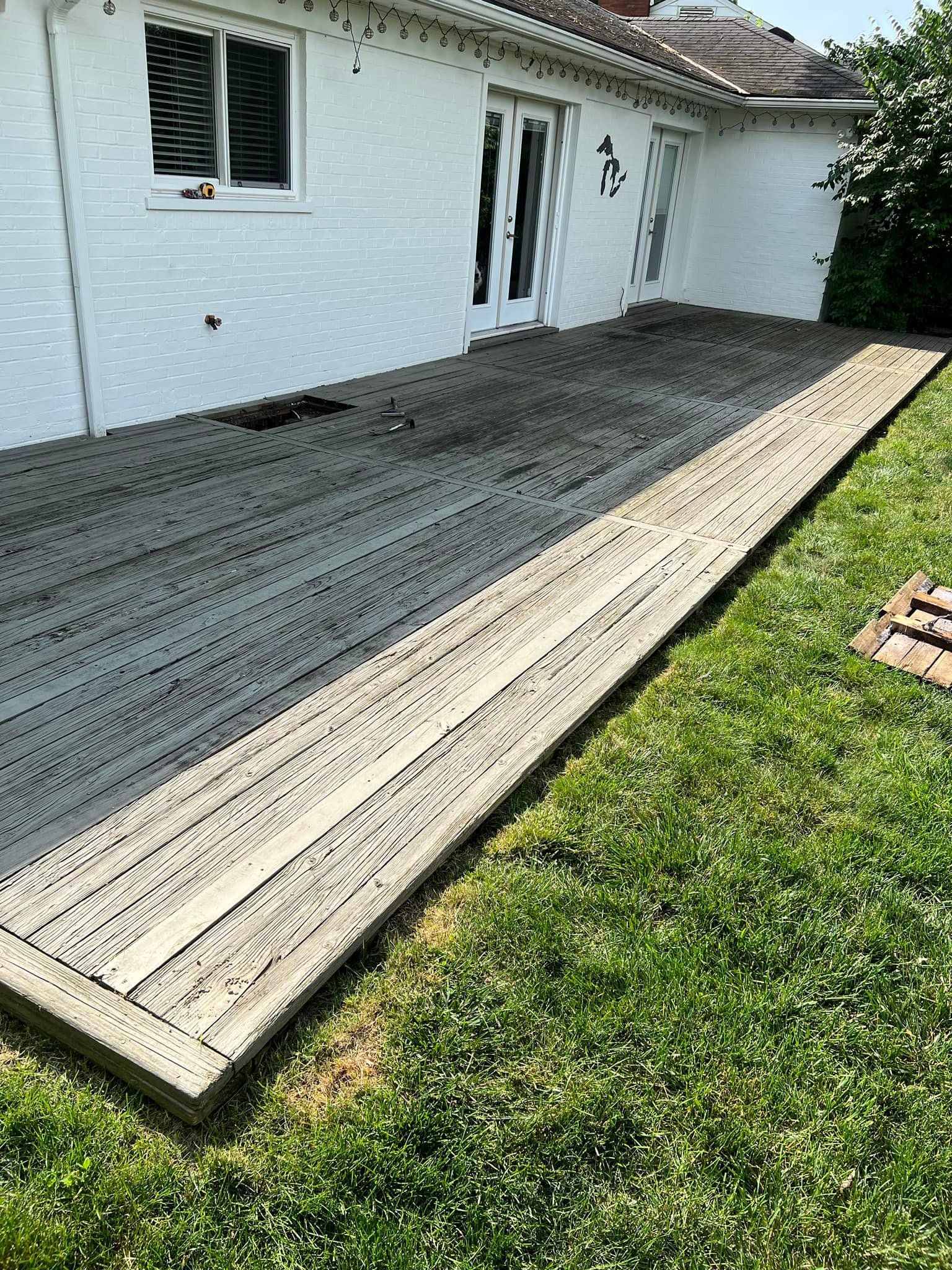 Backyard patio with gray paver work beside a white house and green lawn