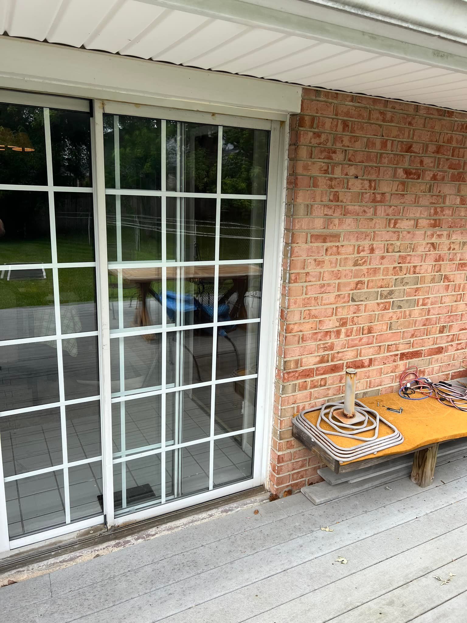 Brick patio with a white-framed glass door, red brick wall, and a small wooden table holding tools.