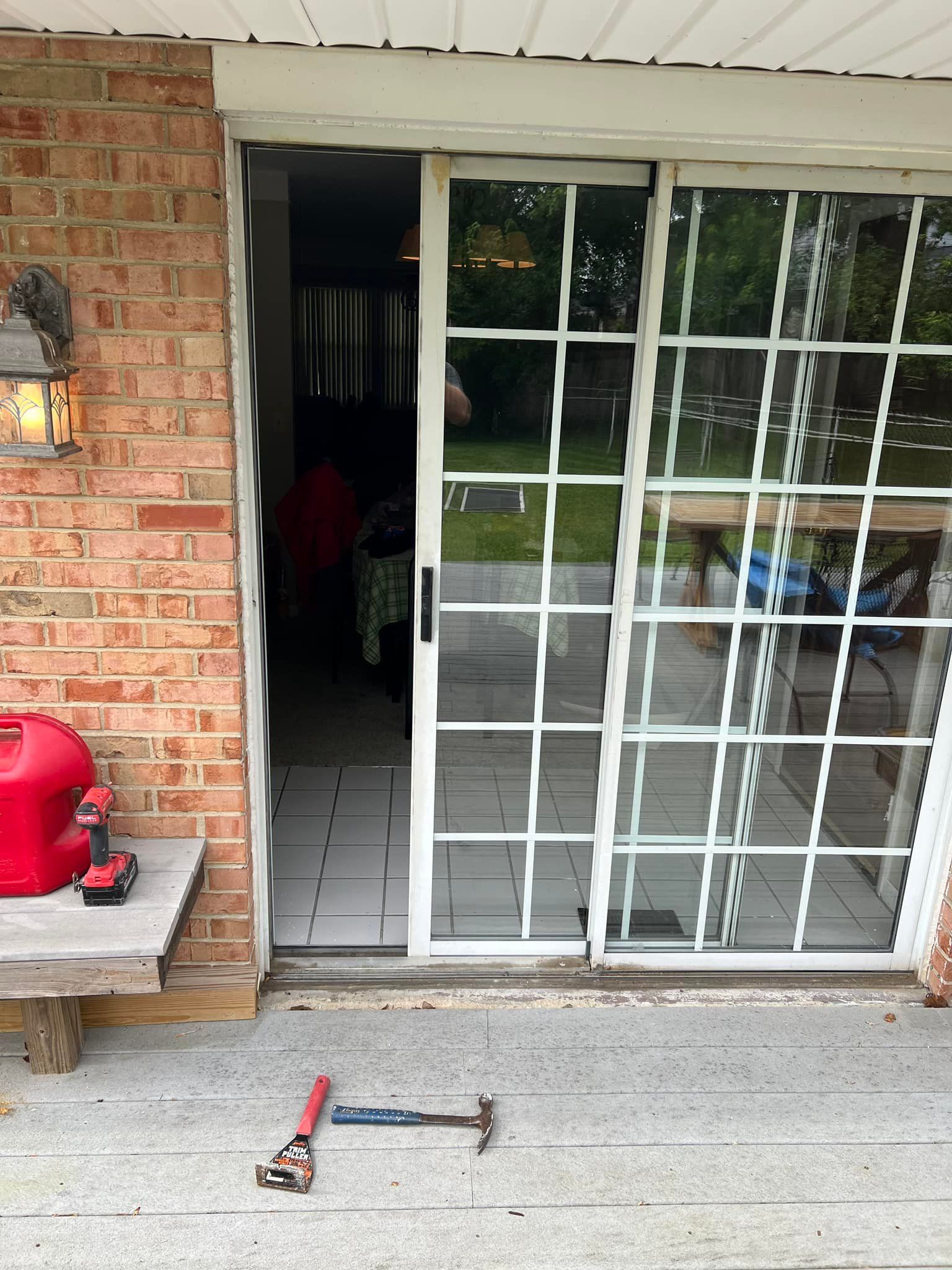 Patio with a white sliding glass door, brick wall, red grill, and a scooter on the concrete floor.