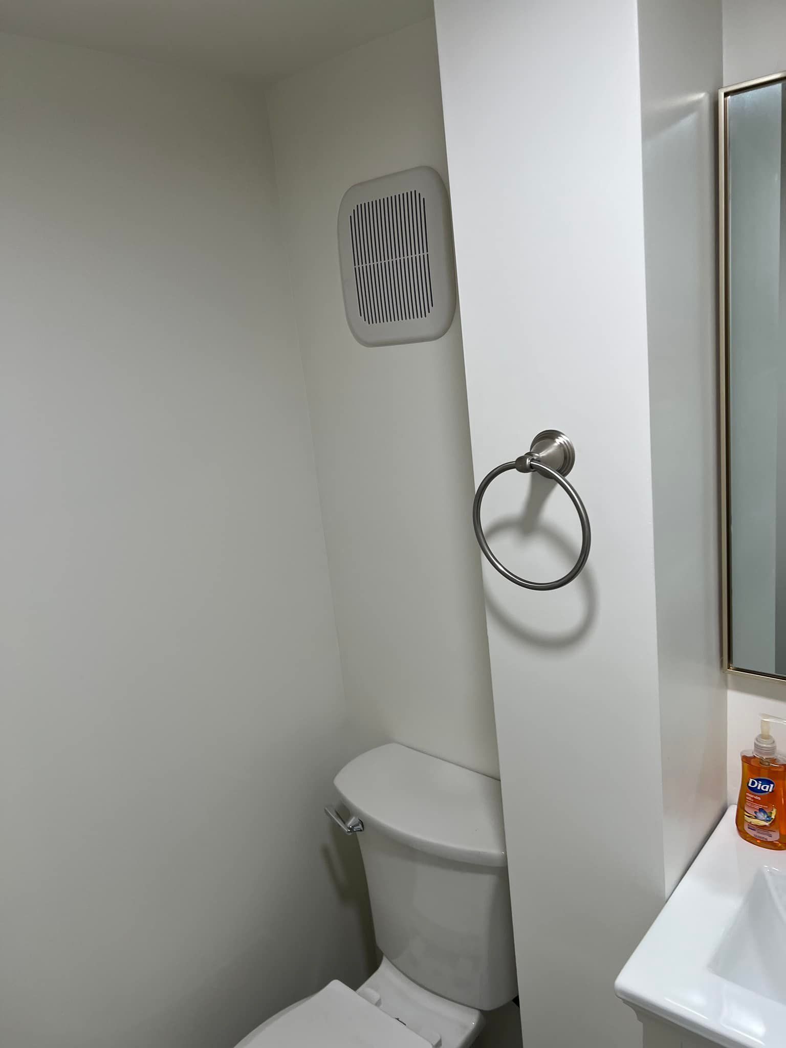 Small bathroom corner with a toilet, towel ring, vent, and sink edge.