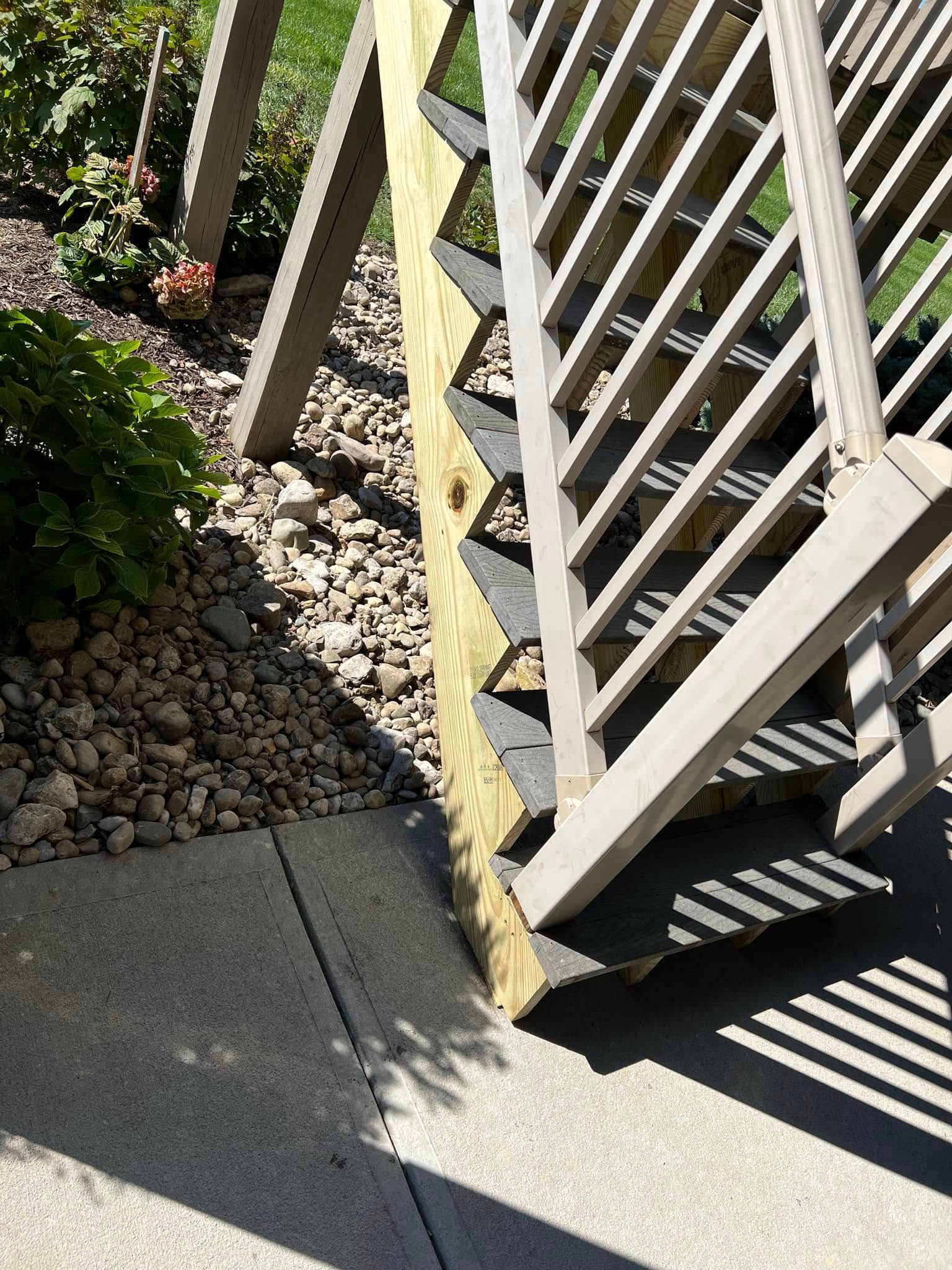 White wooden railing beside a concrete sidewalk and gravel bed in bright sunlight