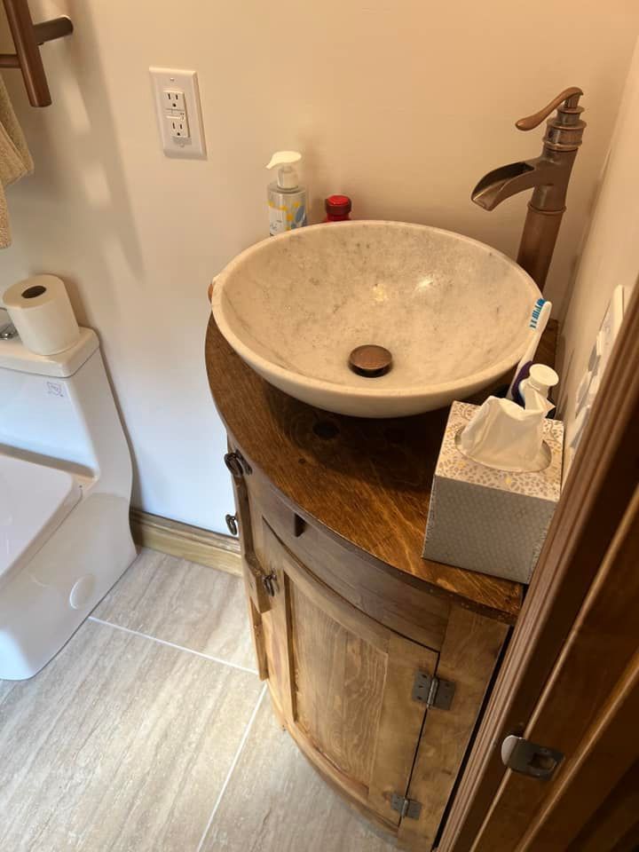 Small bathroom vanity with round stone sink, dark wood cabinet, and toilet at left.