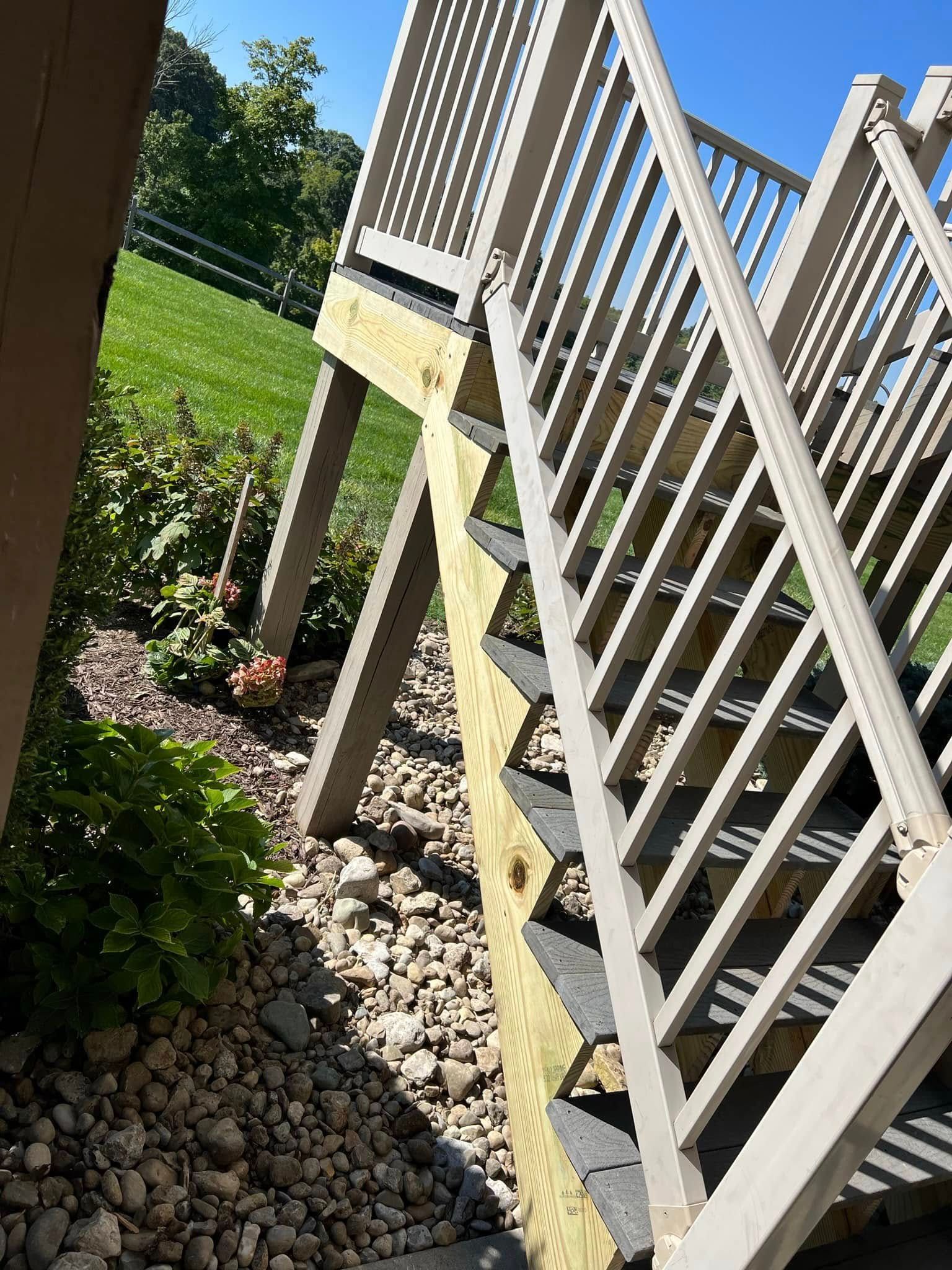 White railing beside a small raised deck over a rock bed in a sunny yard