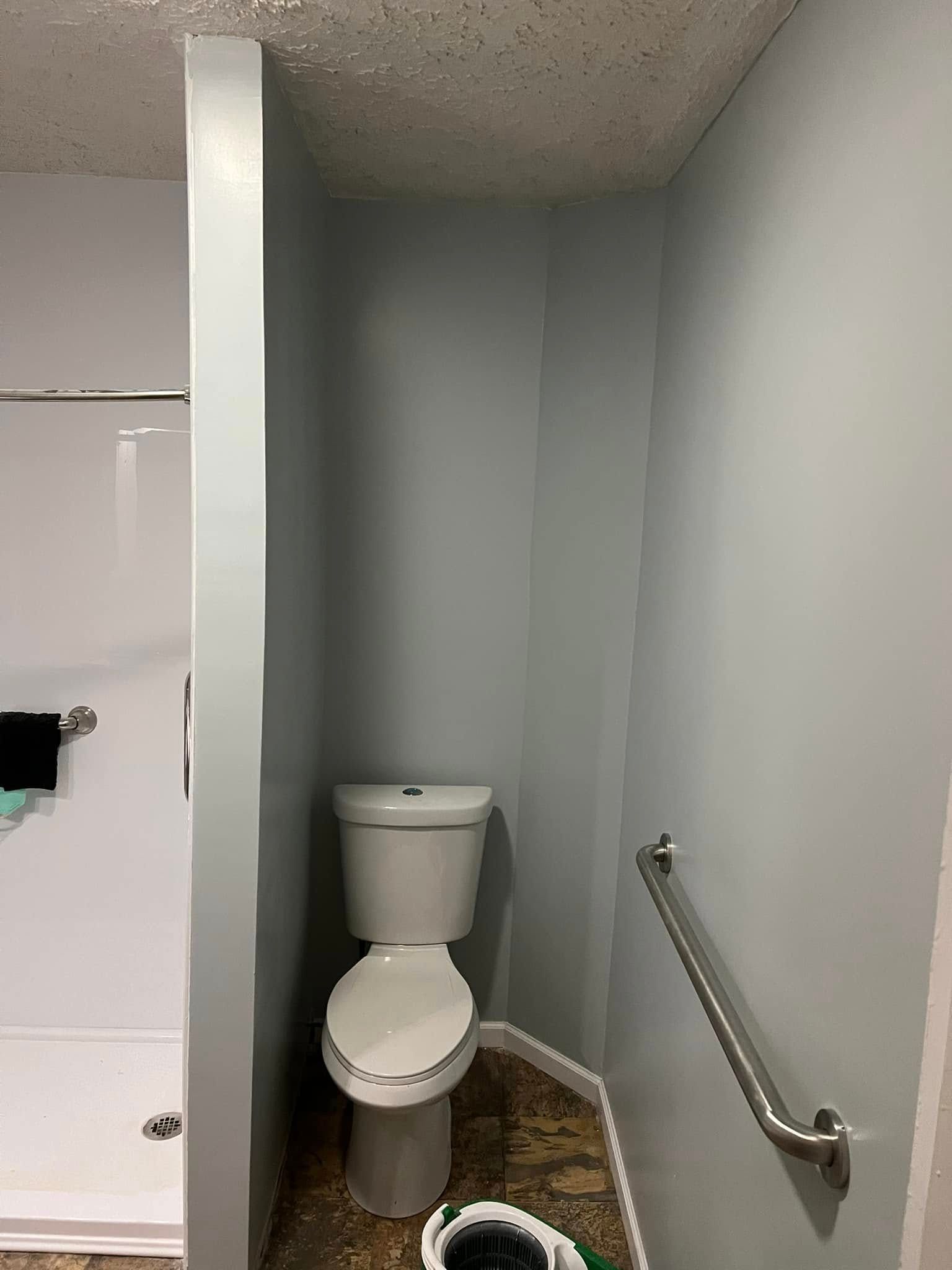 Small restroom with a toilet in a narrow gray corner and a wall-mounted grab bar.