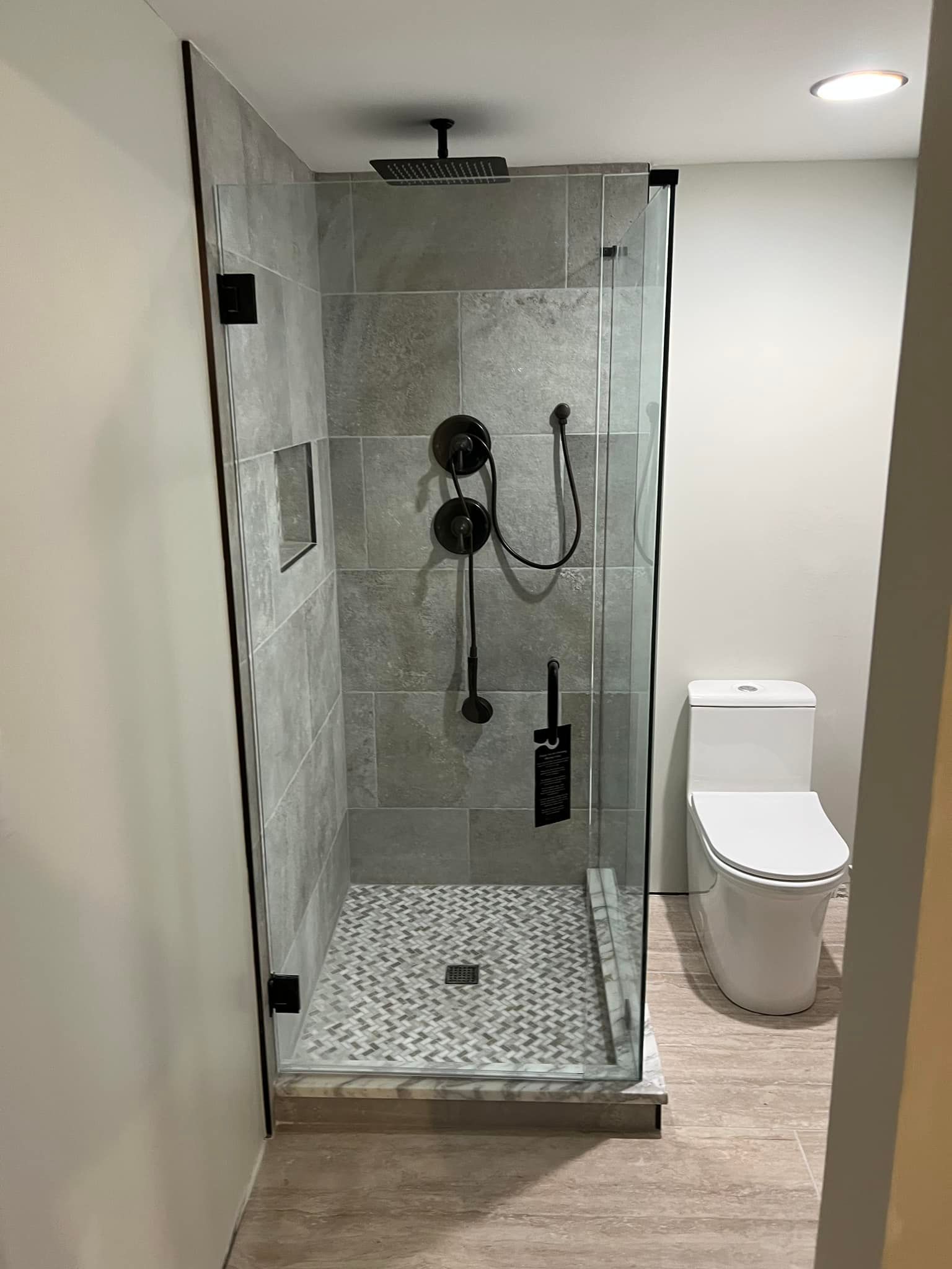 Modern bathroom with glass walk-in shower, mosaic tile floor, and toilet beside it.