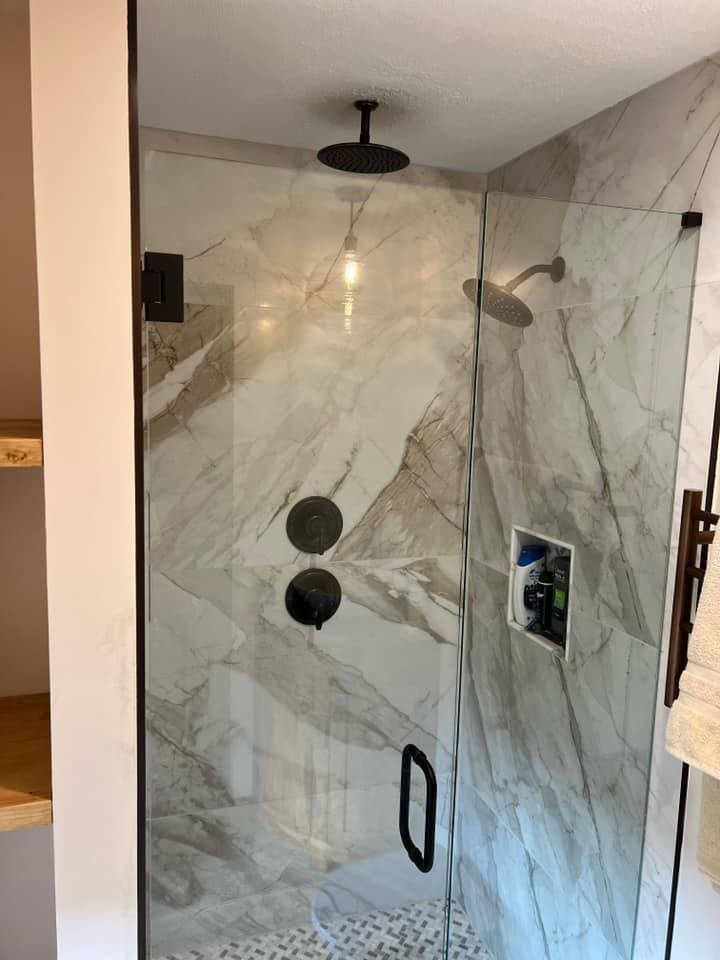 Marble-tiled glass shower stall with black fixtures, recessed niche, and wall-mounted shower head