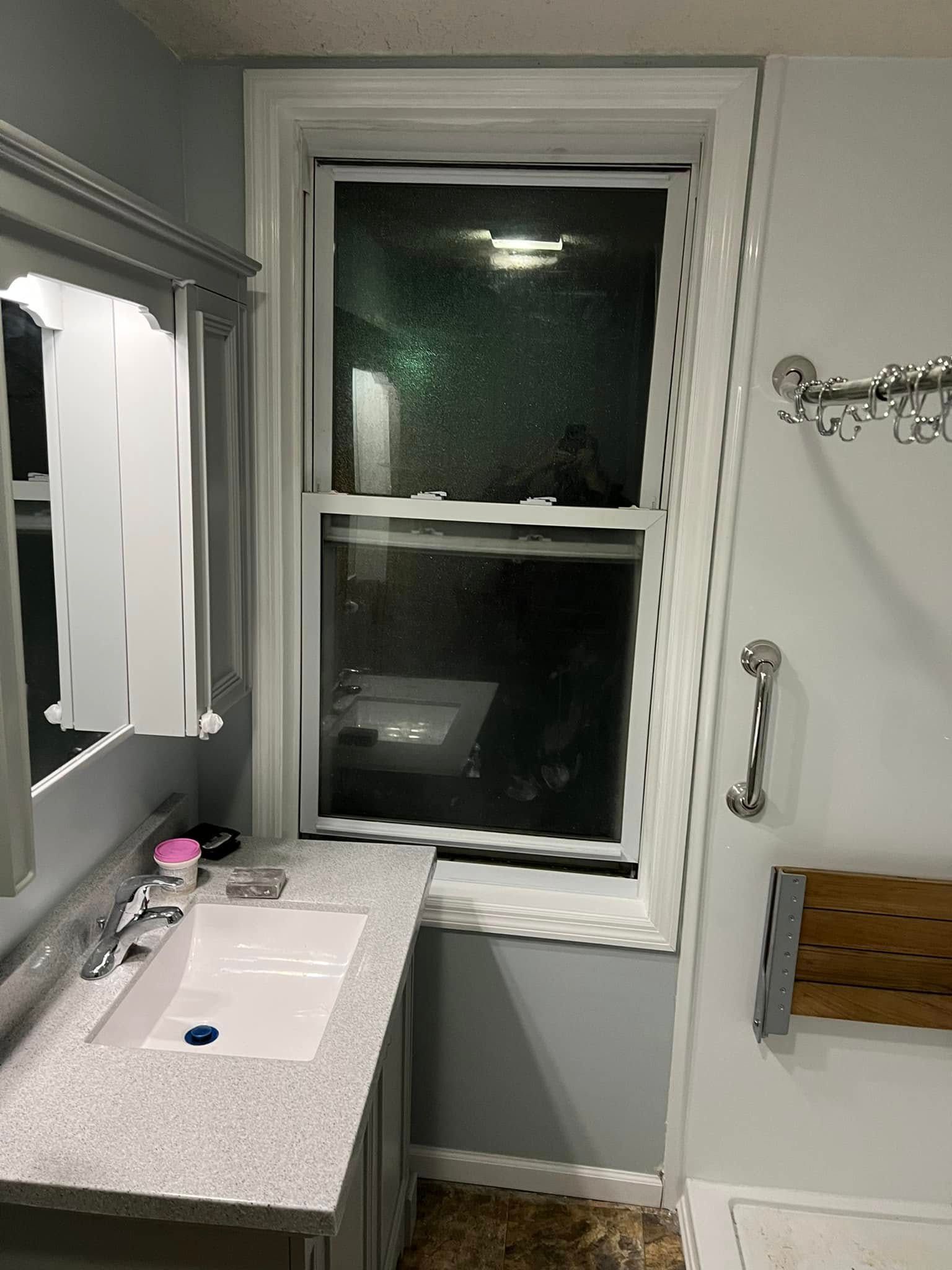 Small bathroom with a sink, mirror, towel rack, and window at night
