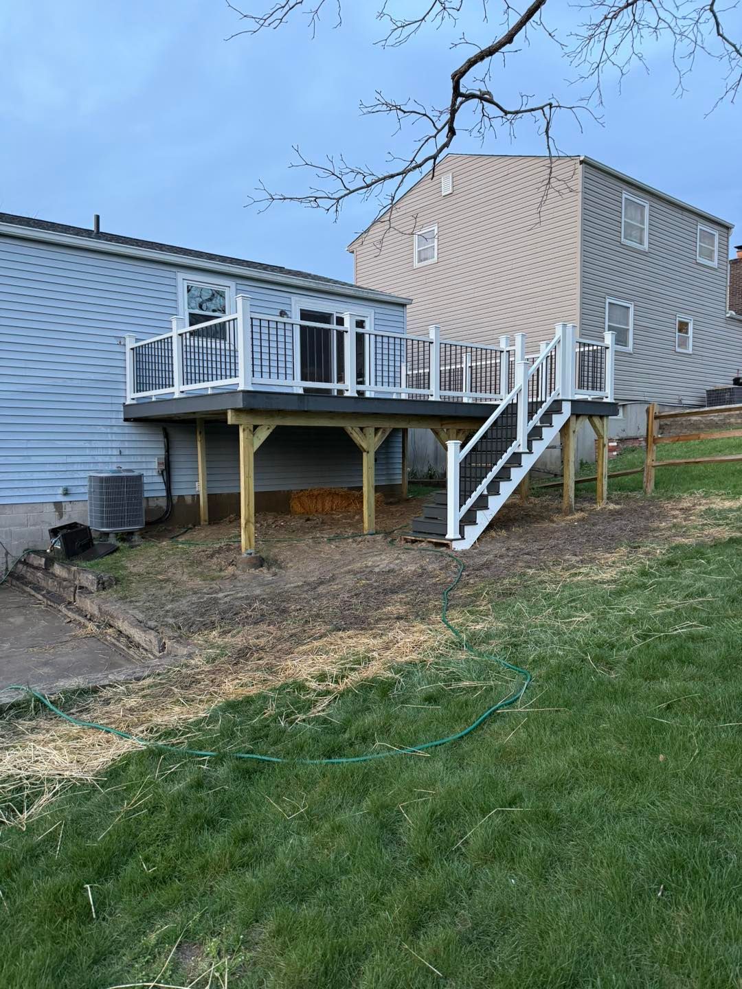 Back deck with stairs on a raised gray house over a dirt yard under a cloudy sky