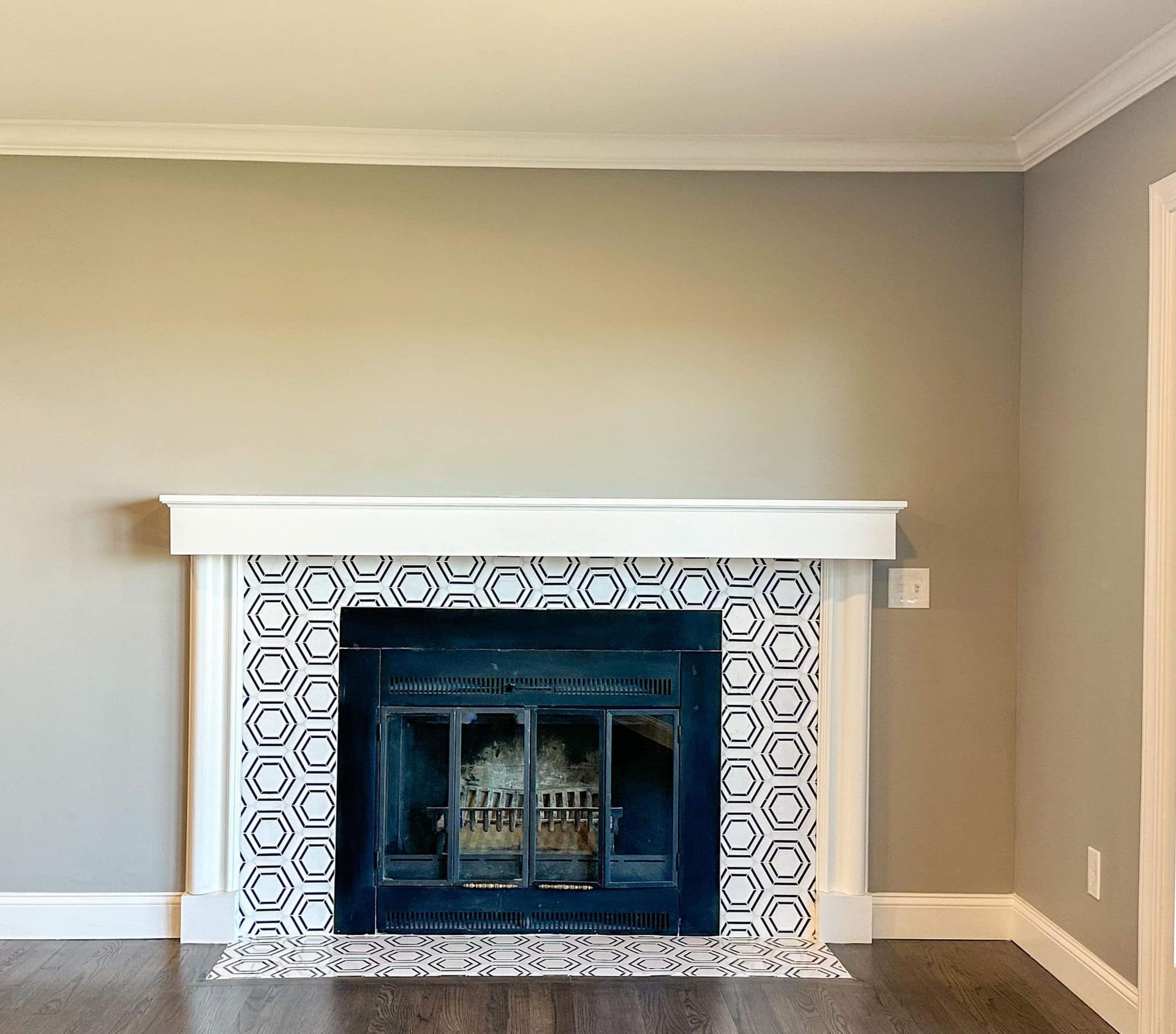 Empty living room with a tiled fireplace, white mantel, beige walls, and dark hardwood floor