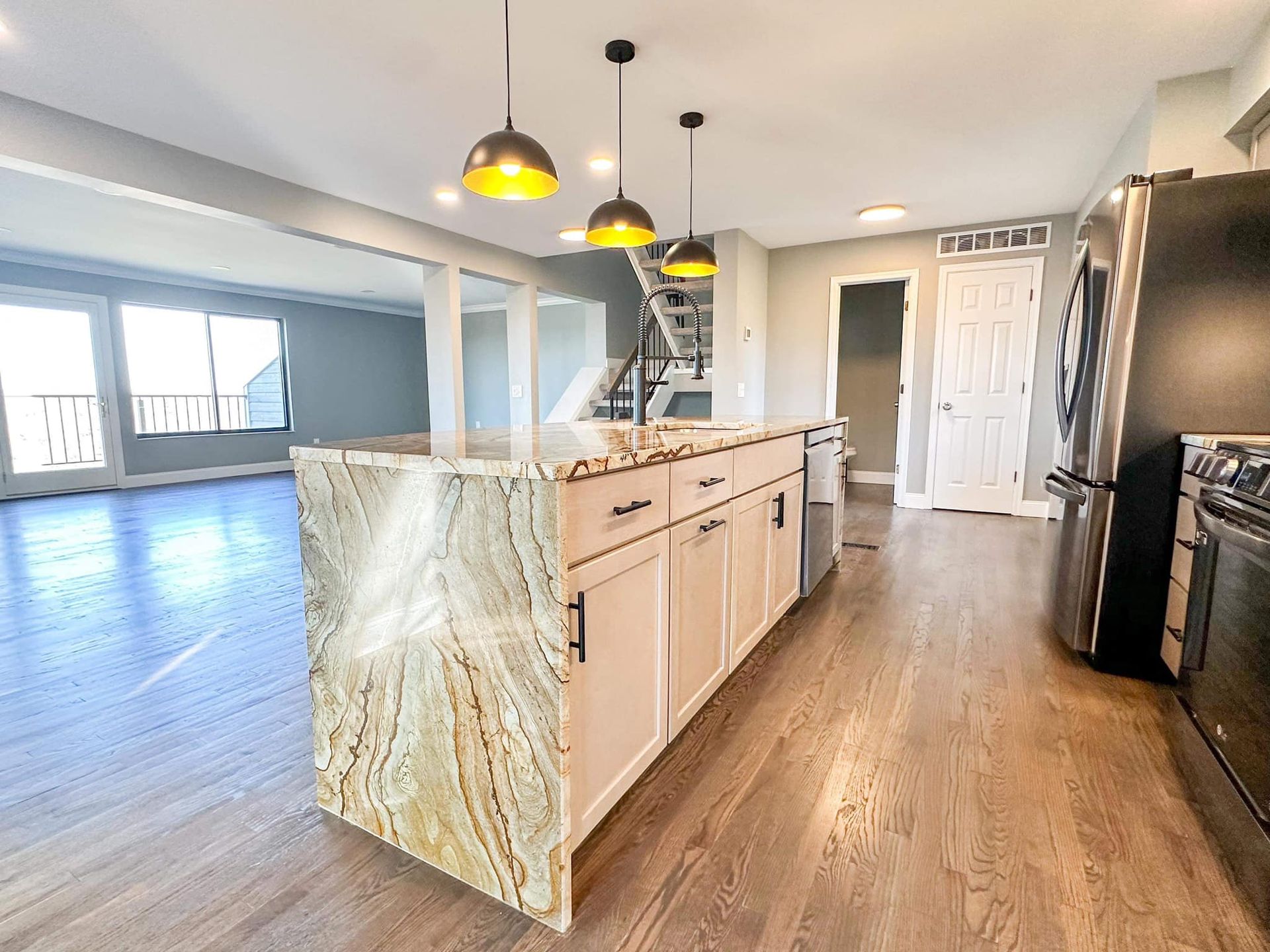 Bright modern kitchen with white cabinets, wood floors, island, and pendant lights opening to a living area