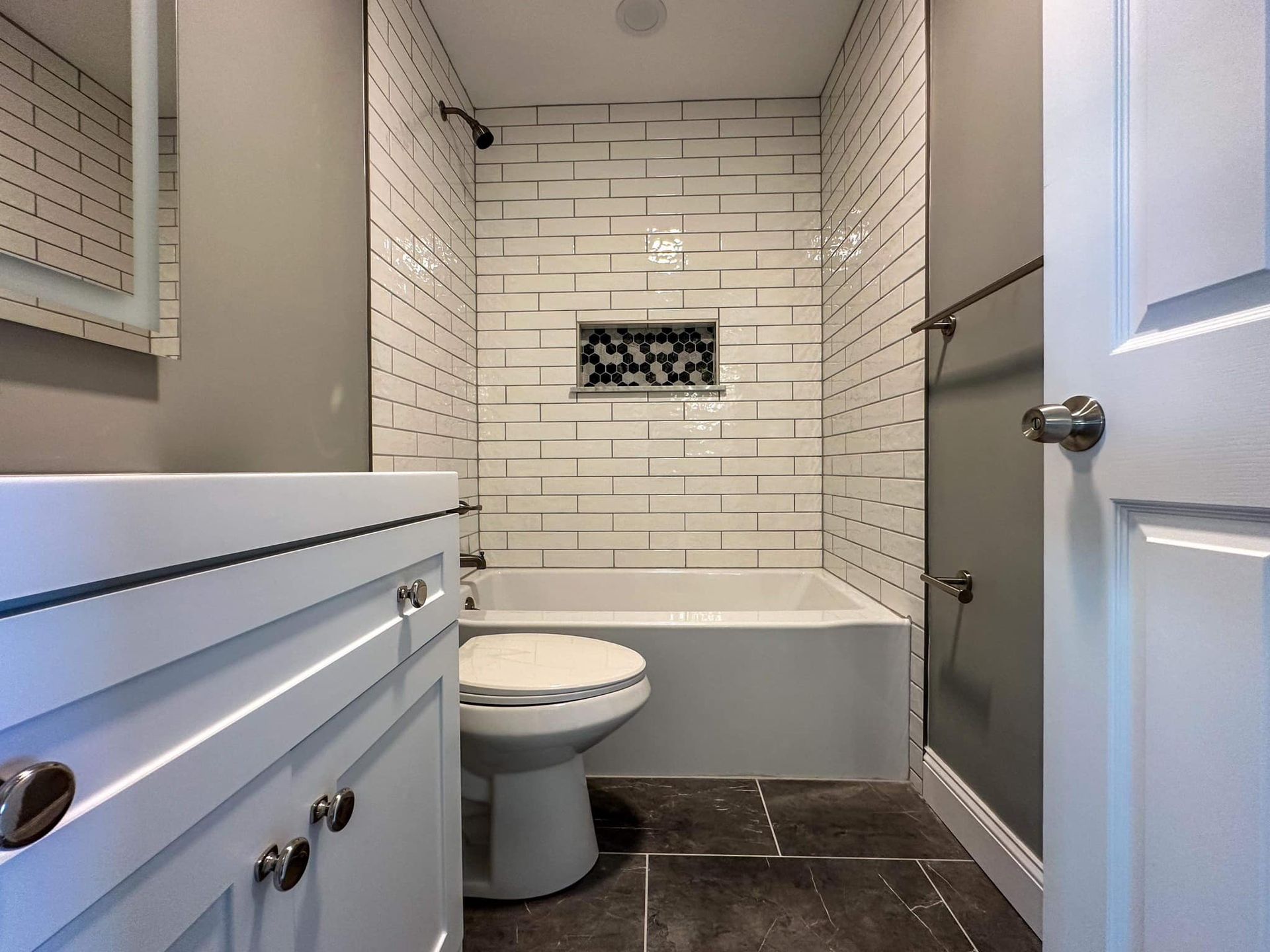 Compact bathroom with white subway-tile shower, tub, toilet, gray walls, and dark tile floor