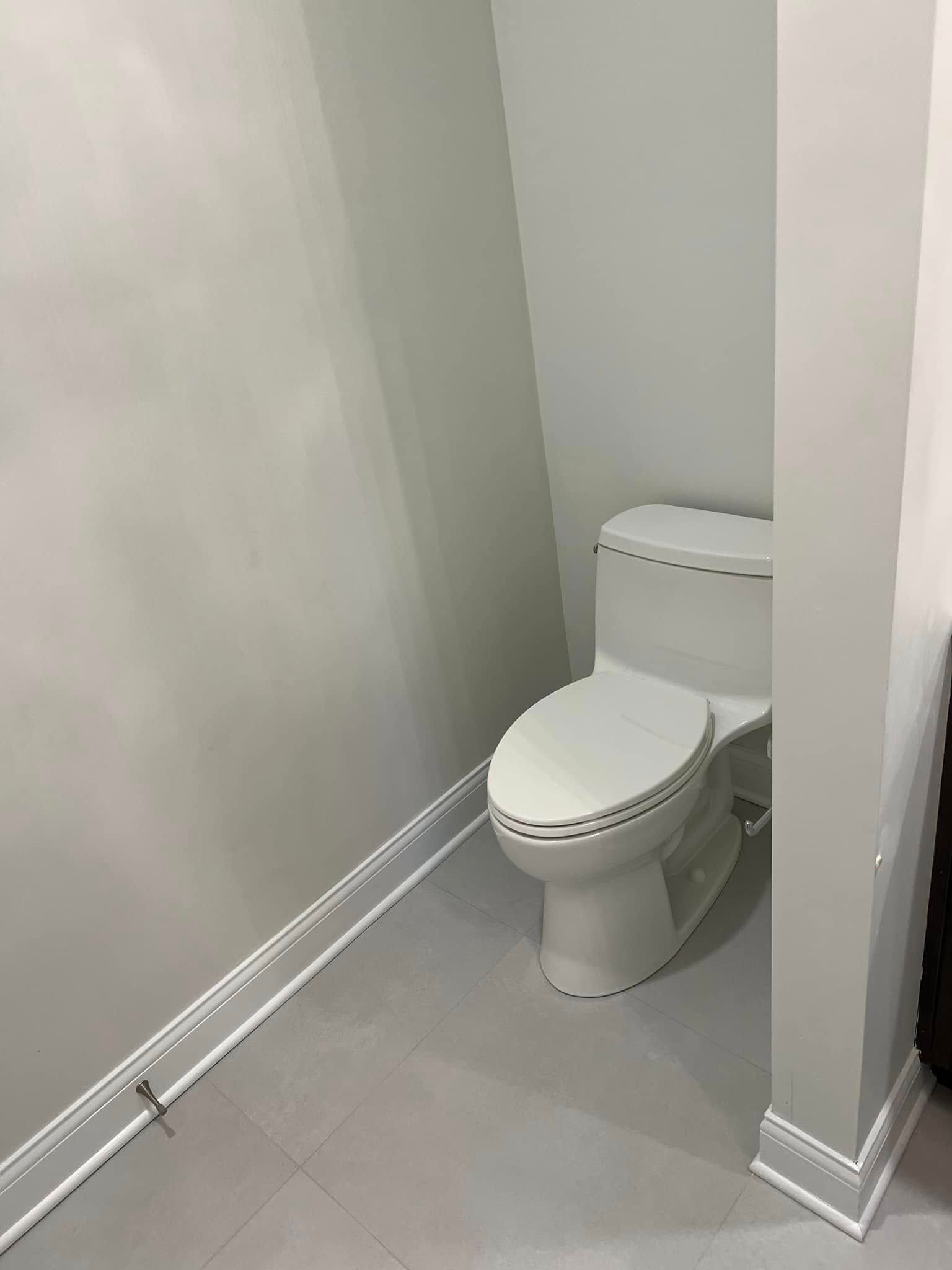 Small bathroom with a white toilet tucked into a narrow corner, gray tile floor and white walls.