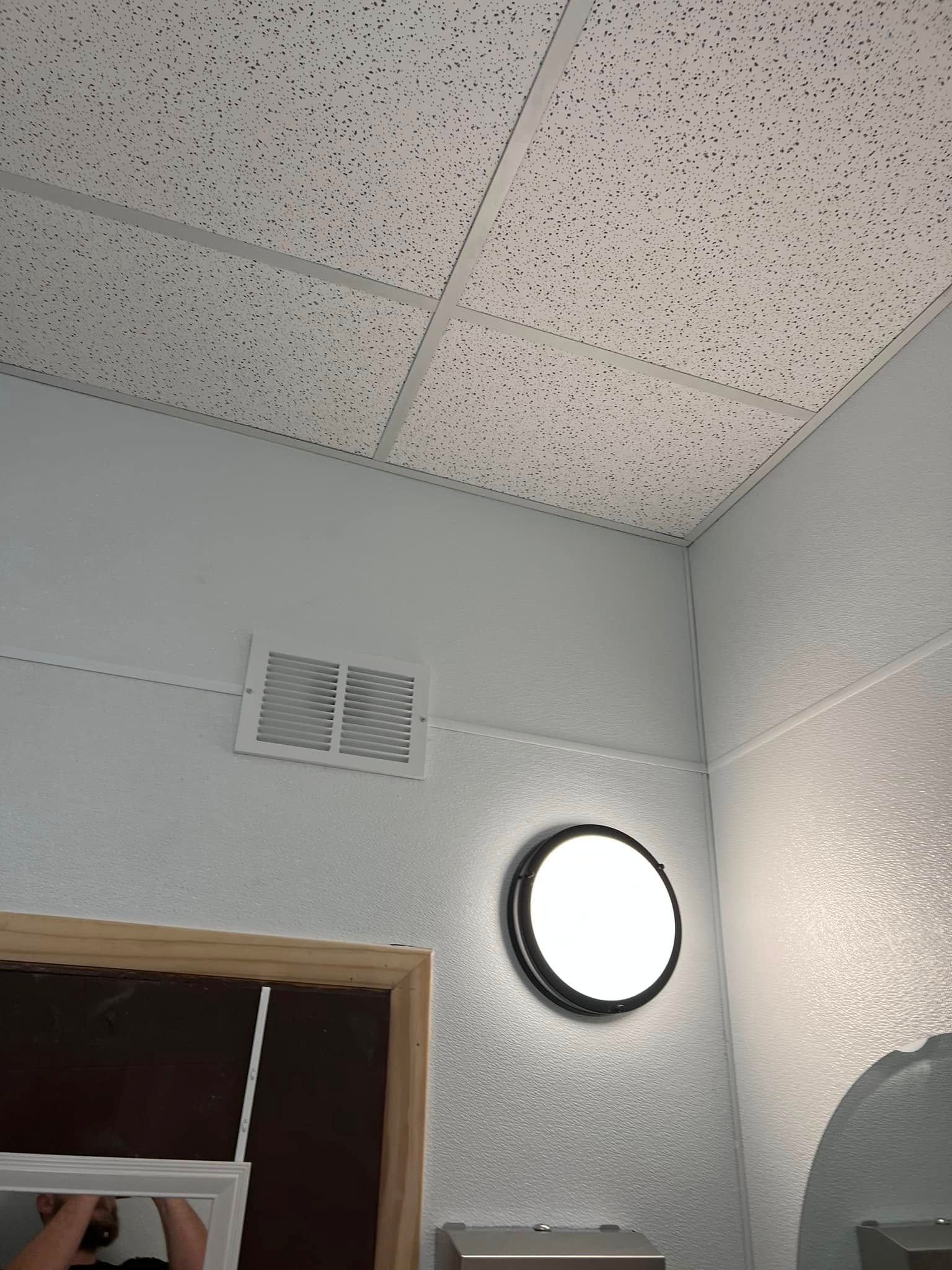 Interior corner with speckled drop ceiling, wall vent, round light, and doorway.