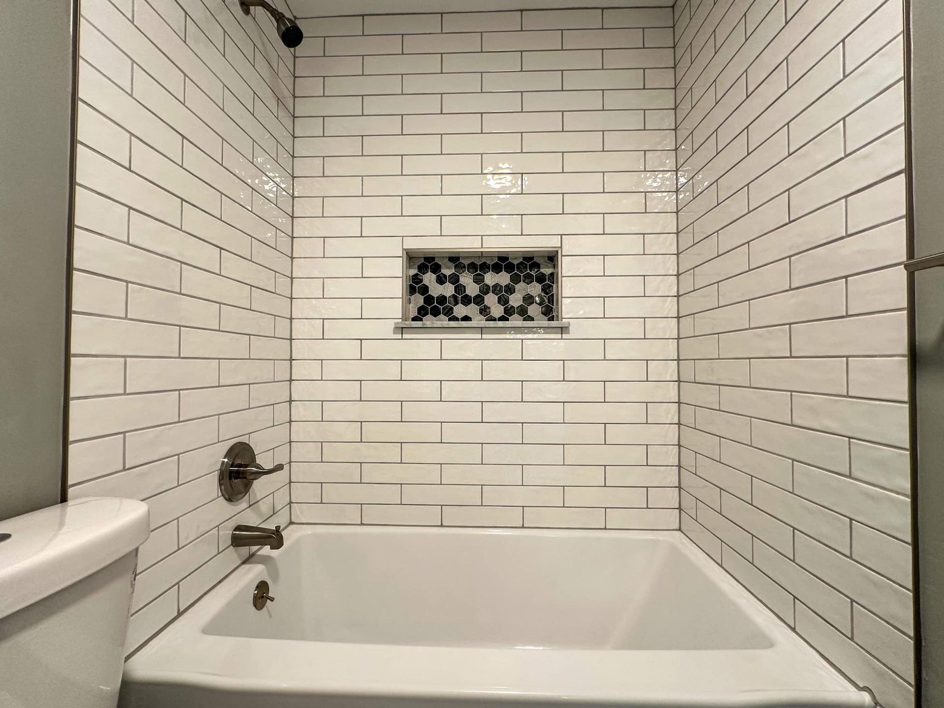 White tiled bathroom with a bathtub, wall faucet, and recessed shelf niche.