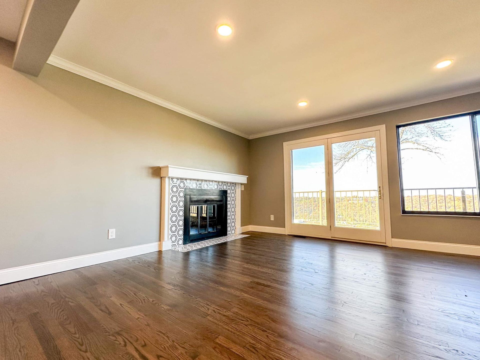 Empty living room with hardwood floors, fireplace, recessed lights, and large glass doors to a patio.