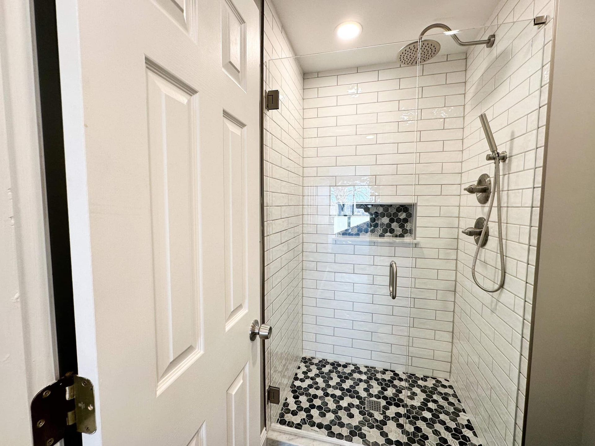 Small tiled shower with white subway walls, black-and-white pebble floor, and chrome showerhead.