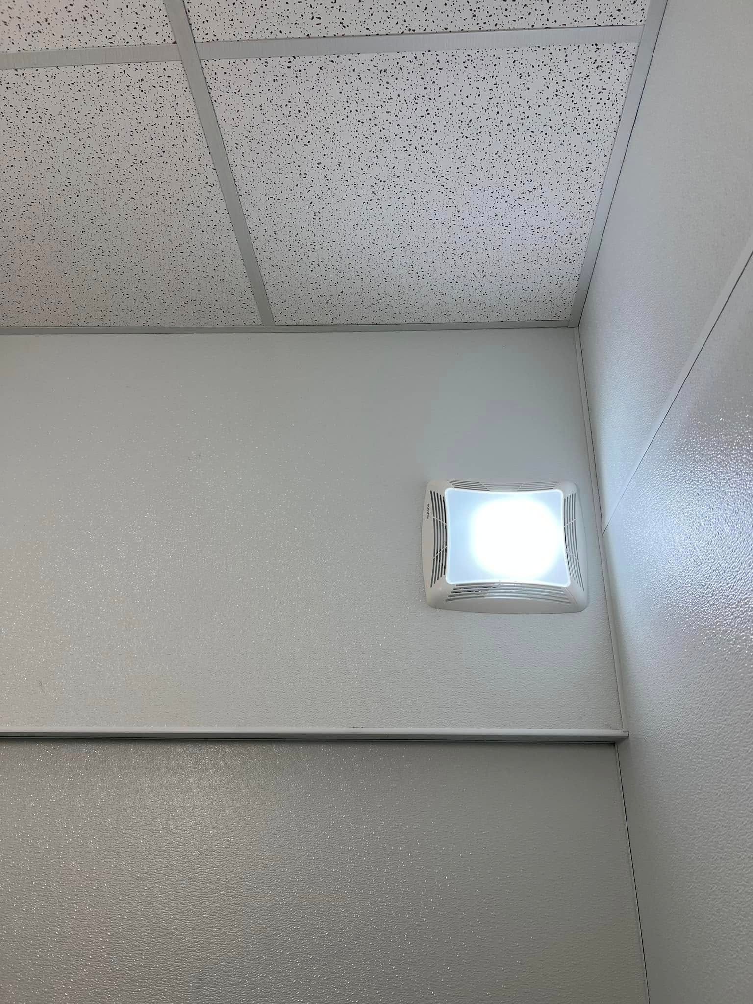 Ceiling corner with a lit wall-mounted light and speckled acoustic tiles