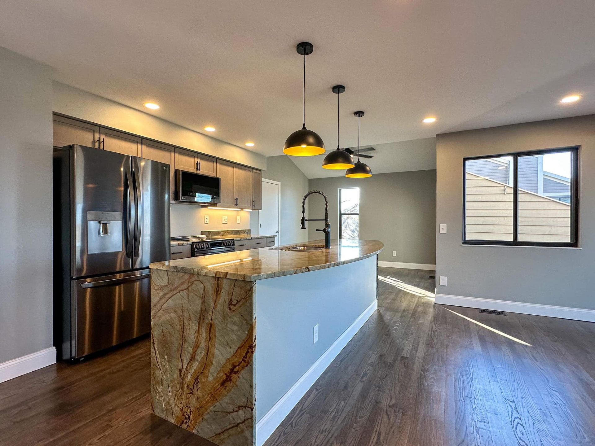 Modern kitchen and dining area with island, stainless fridge, pendant lights, and wood floors