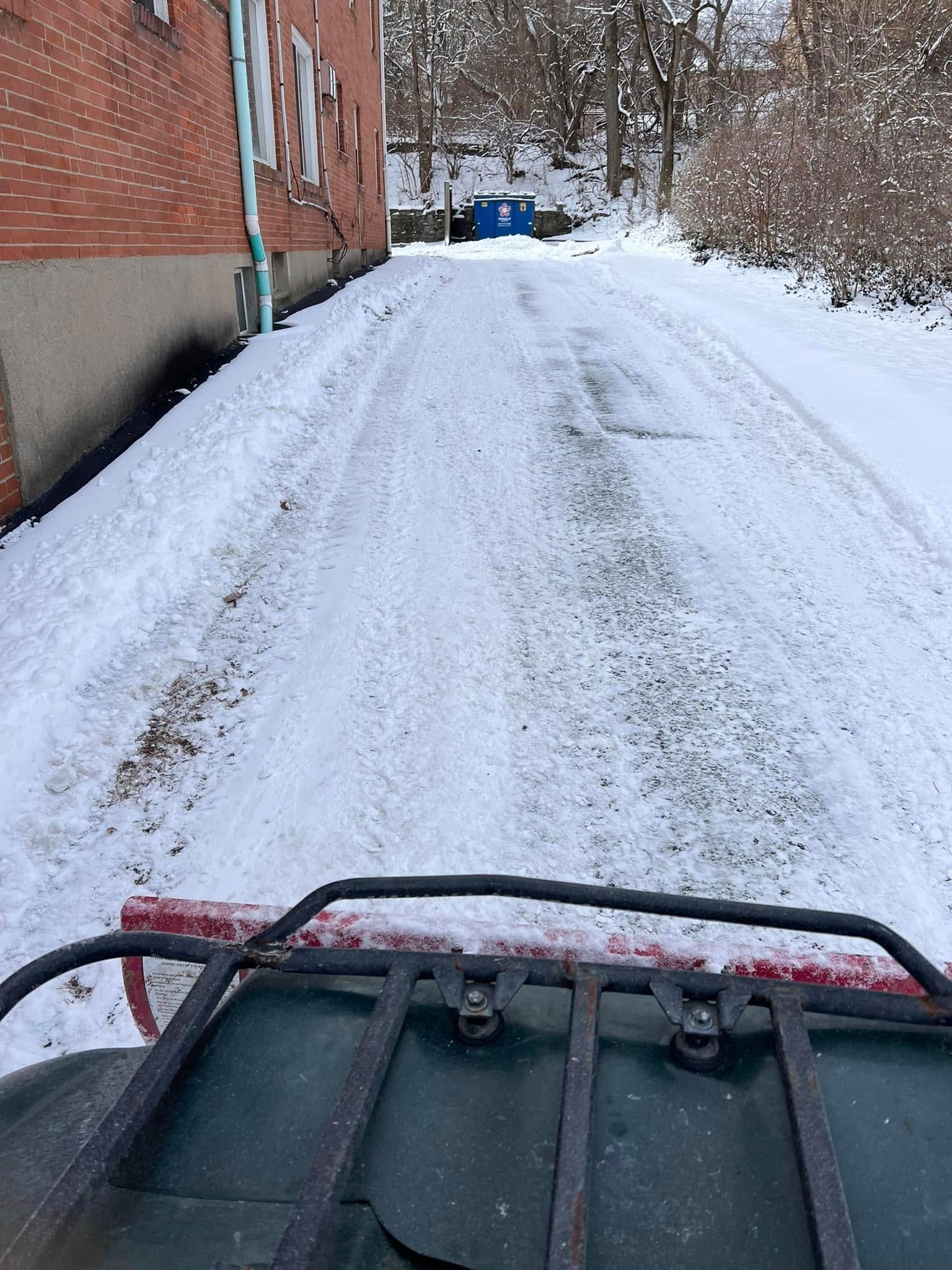 Snow-covered alley beside a brick building, seen from a vehicle with handlebars in the foreground.
