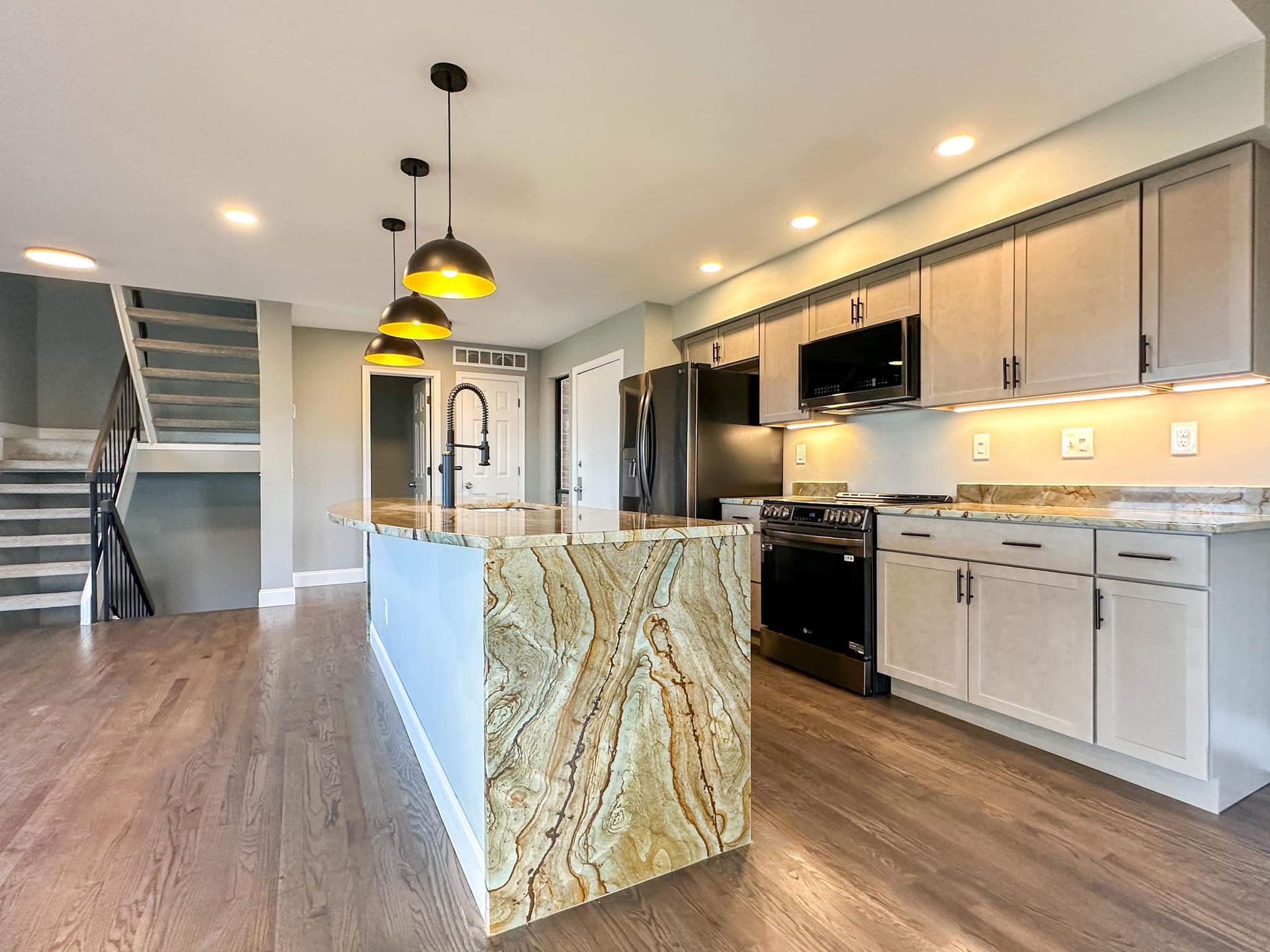 Modern open-plan kitchen with marble island, white cabinets, black appliances, and pendant lights