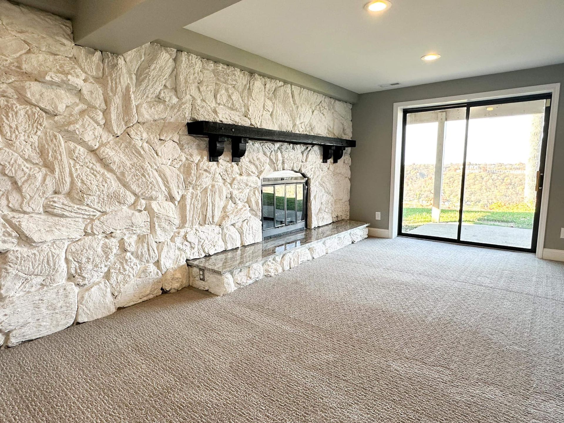 Carpeted living room with stone fireplace wall and large sliding glass doors to a patio.