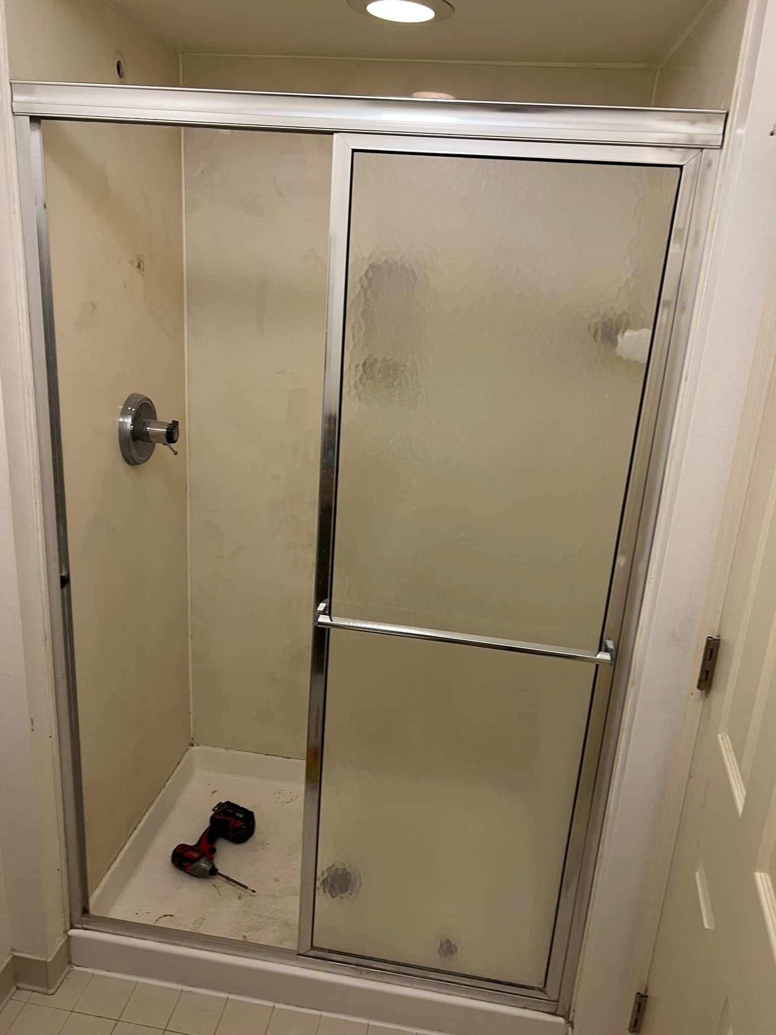 Small bathroom with shower stall and frosted glass sliding door; drill on the shower floor.