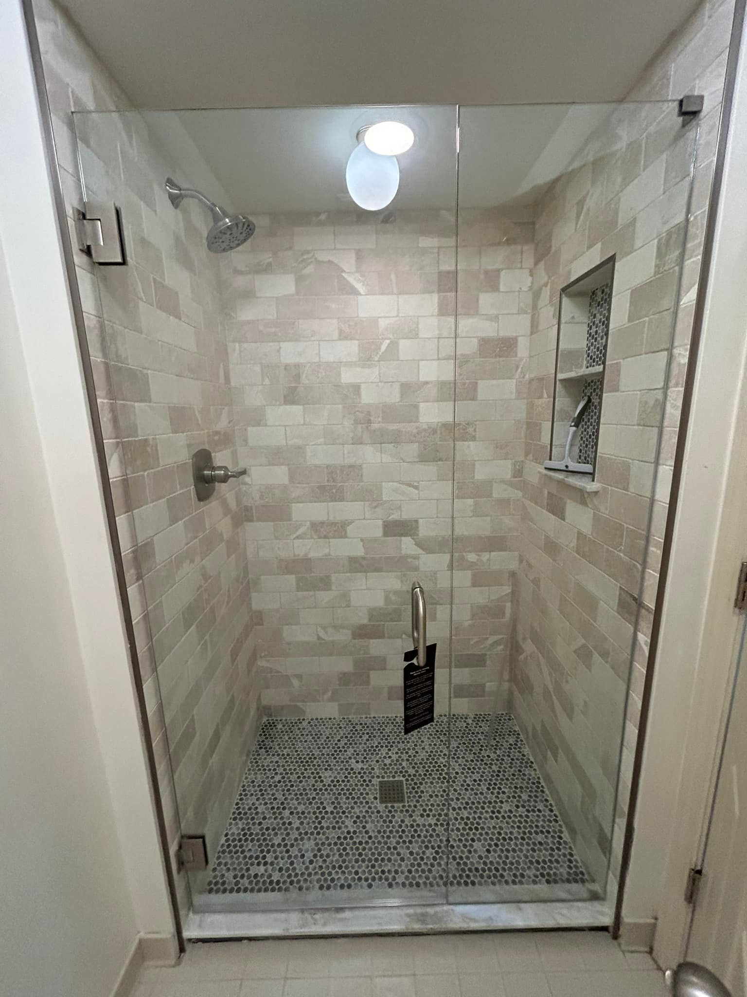 Small tiled walk-in shower with glass doors, beige walls, and a pebble floor.