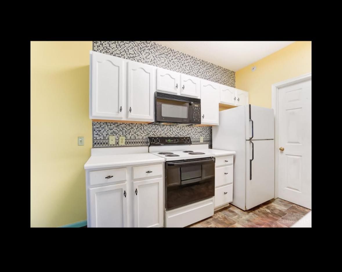 White kitchen with cabinets, black stove and microwave, white refrigerator, and light yellow walls.